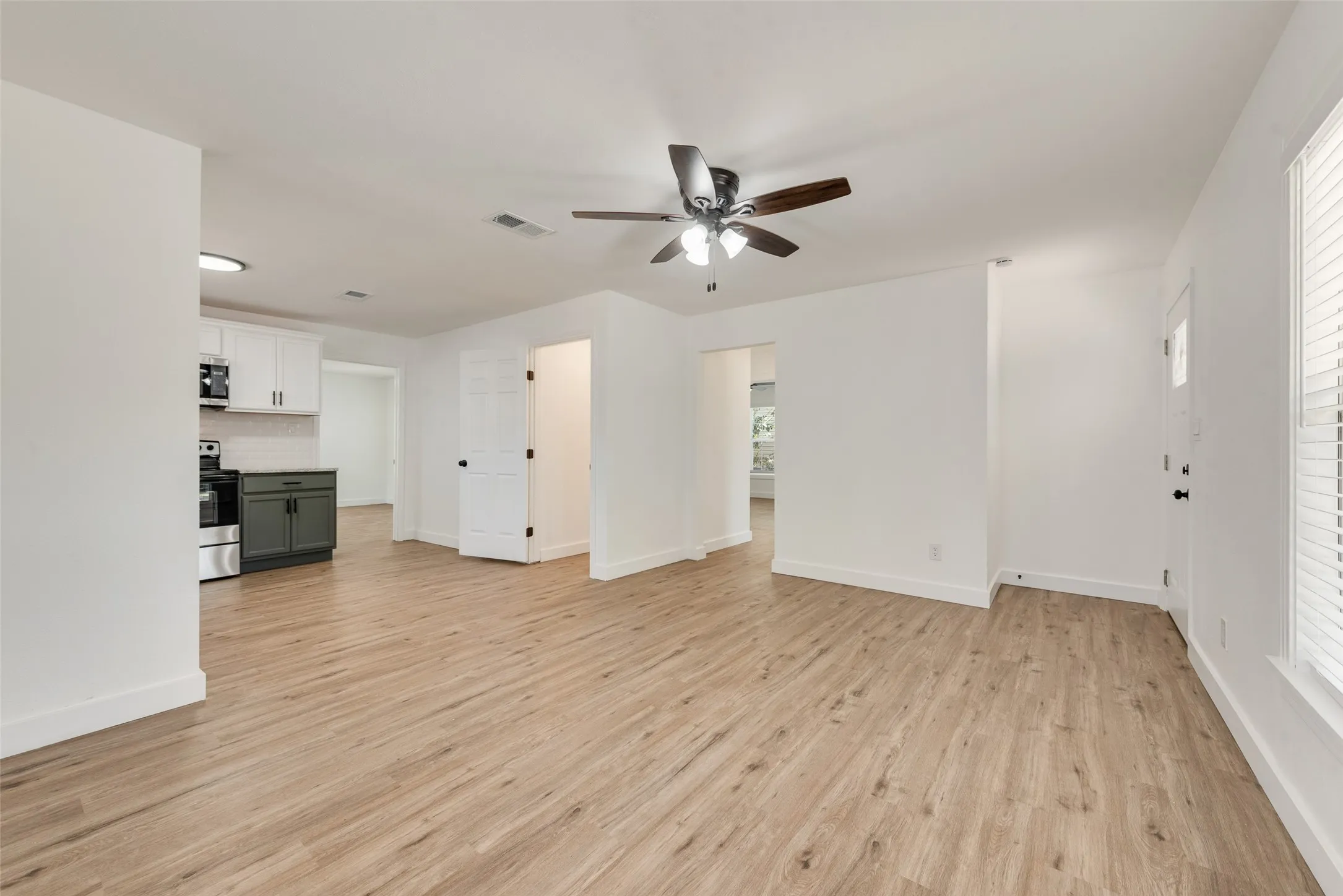 Wood-finish flooring throughout, bright white walls, modern ceiling fan, and white window blinds