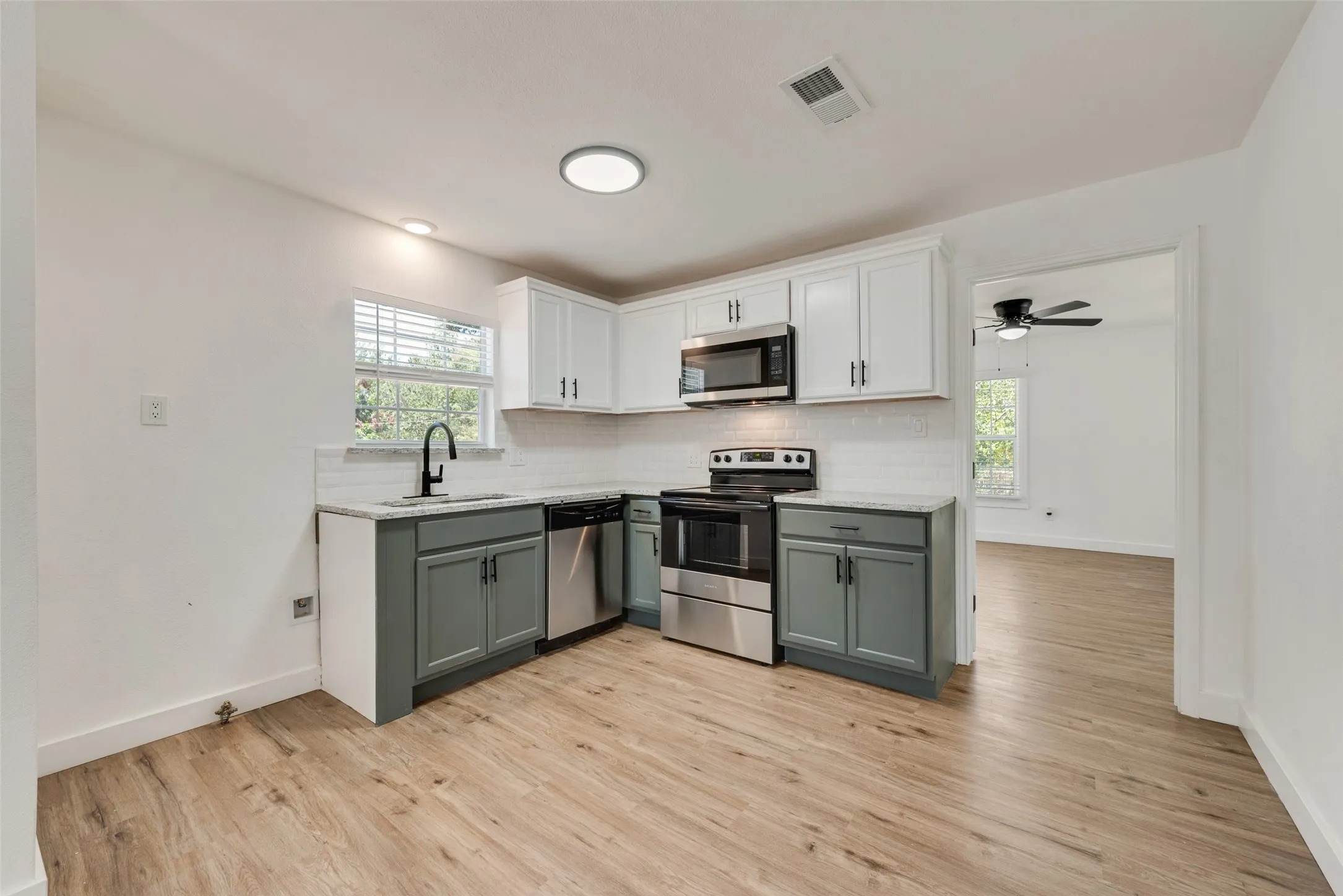 Kitchen featuring stainless steel appliances, wood-finish flooring, white upper cabinetry, and contrasting lower cabinetry