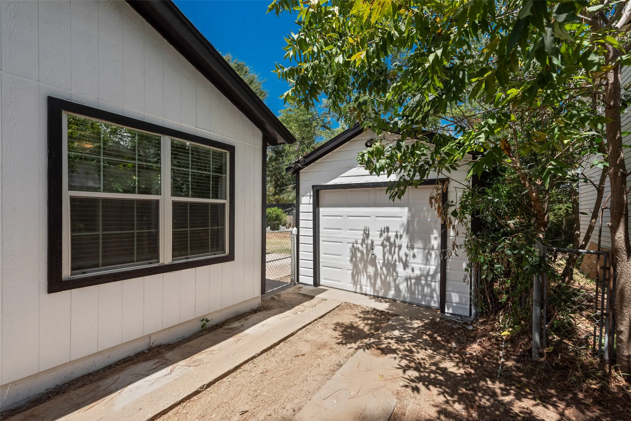 White vertical siding exterior with dark trim, window with blinds, and attached garage
