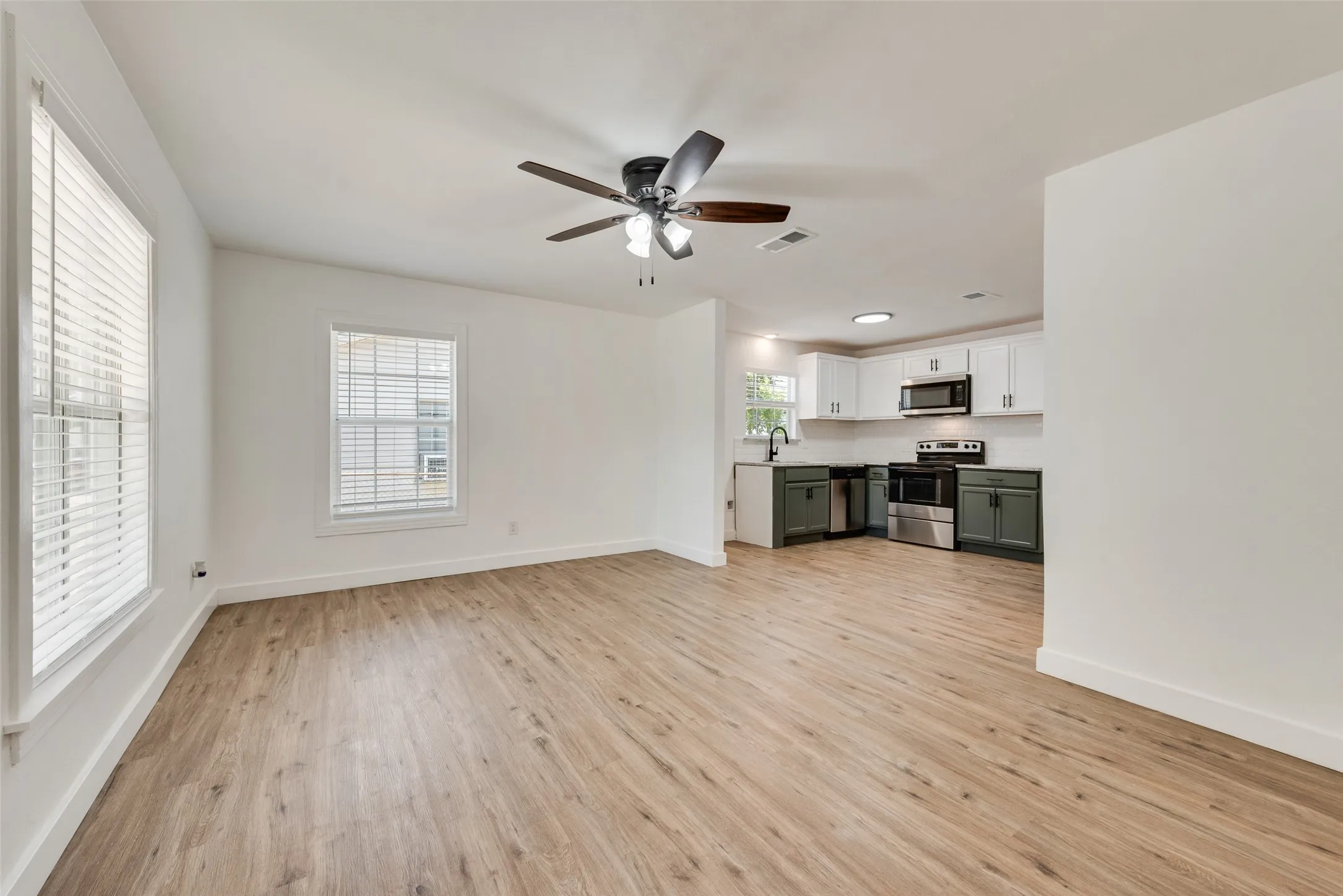 Open-concept living area with wood-finish flooring, ceiling fan, and white walls