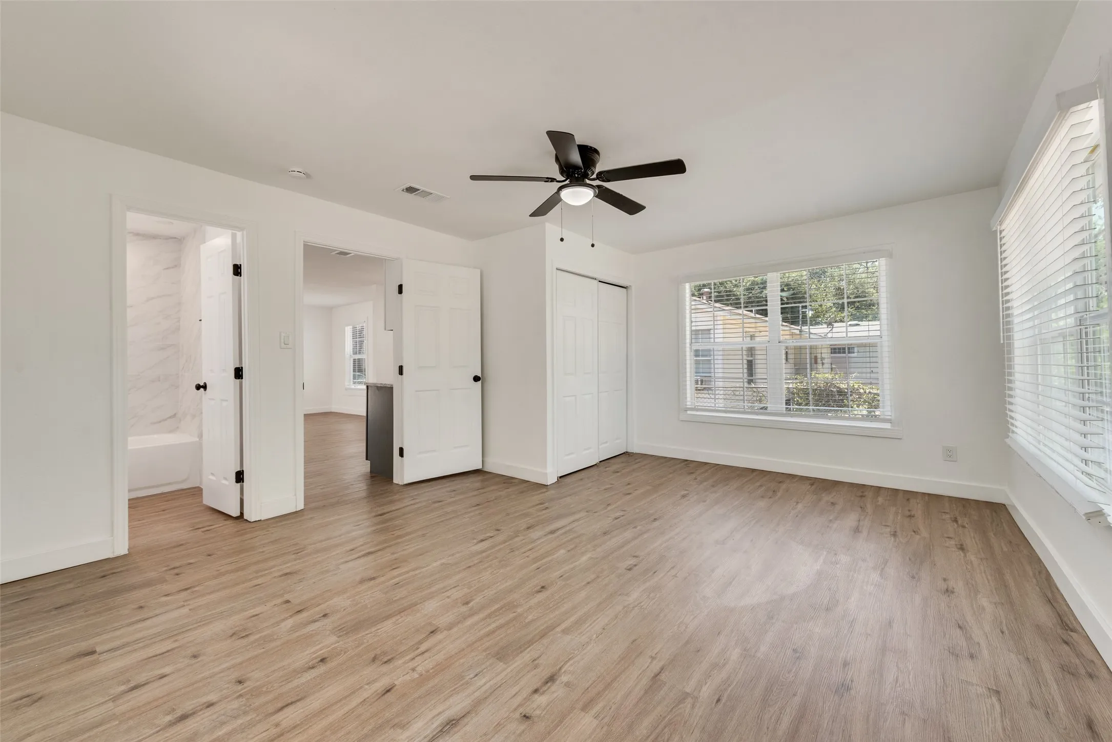Wood-finish flooring, white walls, and a black ceiling fan with an integrated light fixture