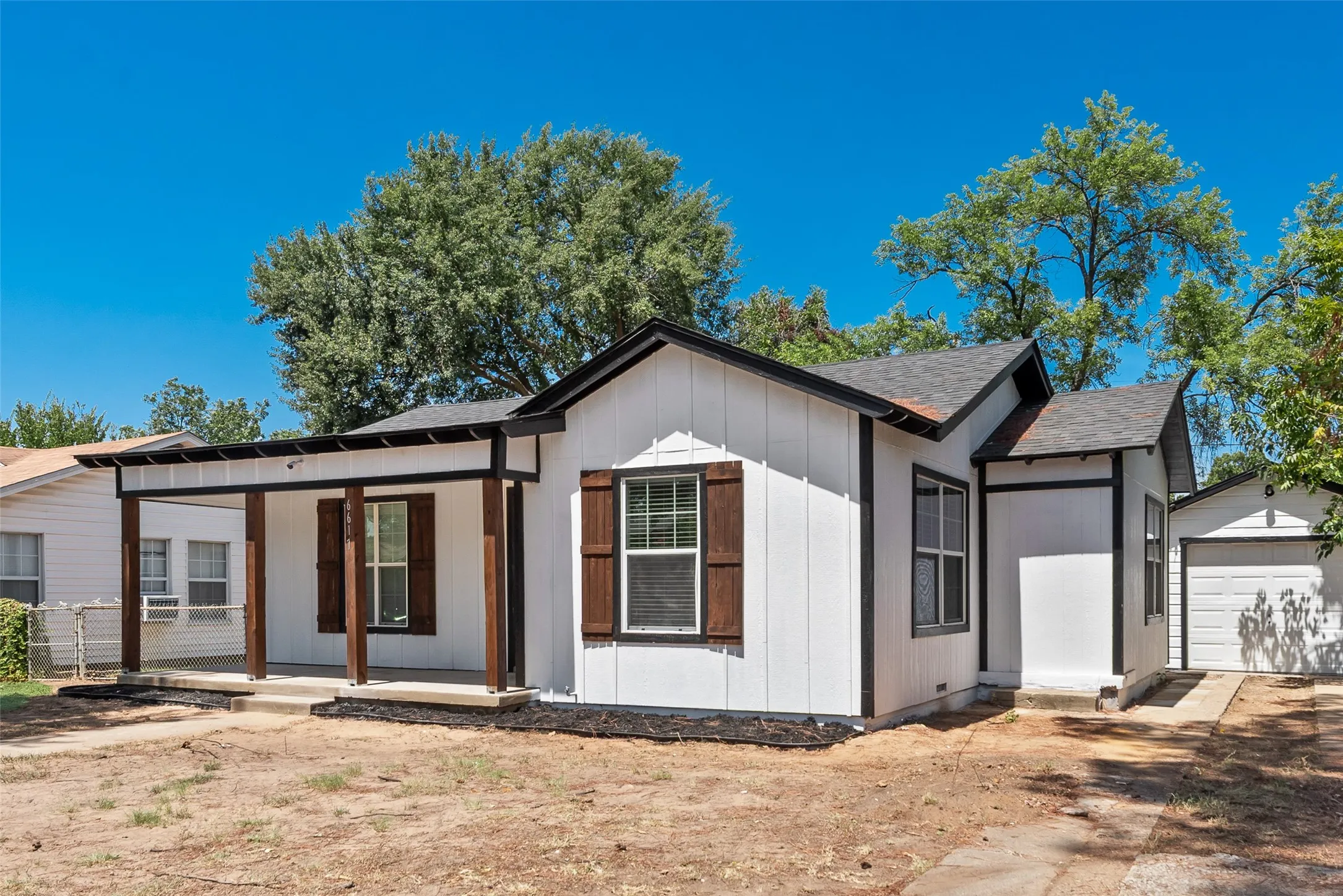 White vertical siding exterior with dark trim accents, covered front porch with wood-finish columns, and a detached garage with a white panel door