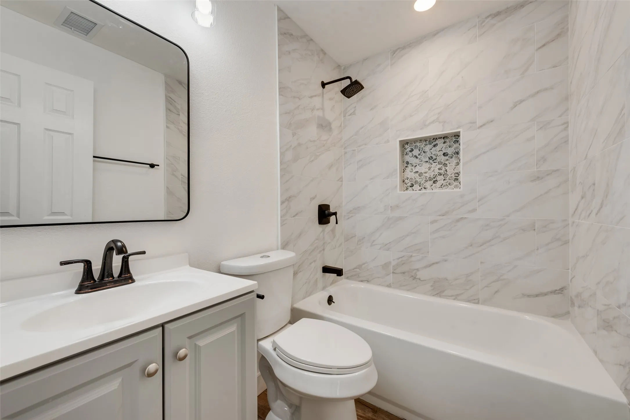 Bathroom featuring a shower/tub combination with tiled surround, a built-in shower niche, a single vanity with a white countertop, and a framed mirror