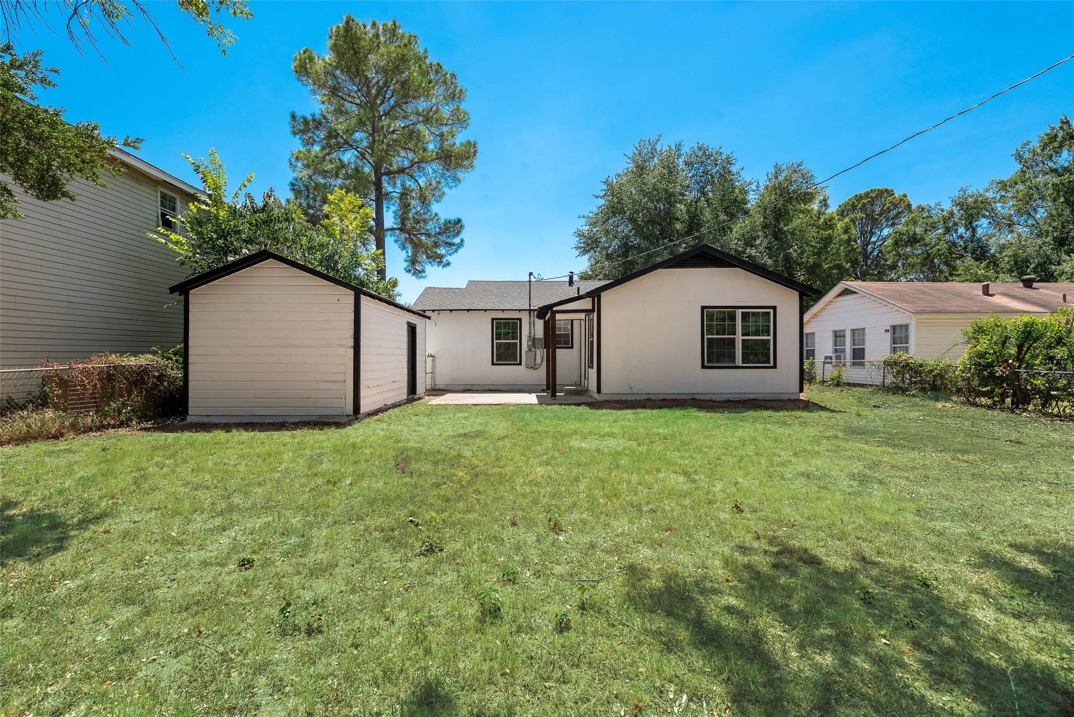 Expansive backyard featuring a manicured lawn, a detached storage building, and a concrete patio