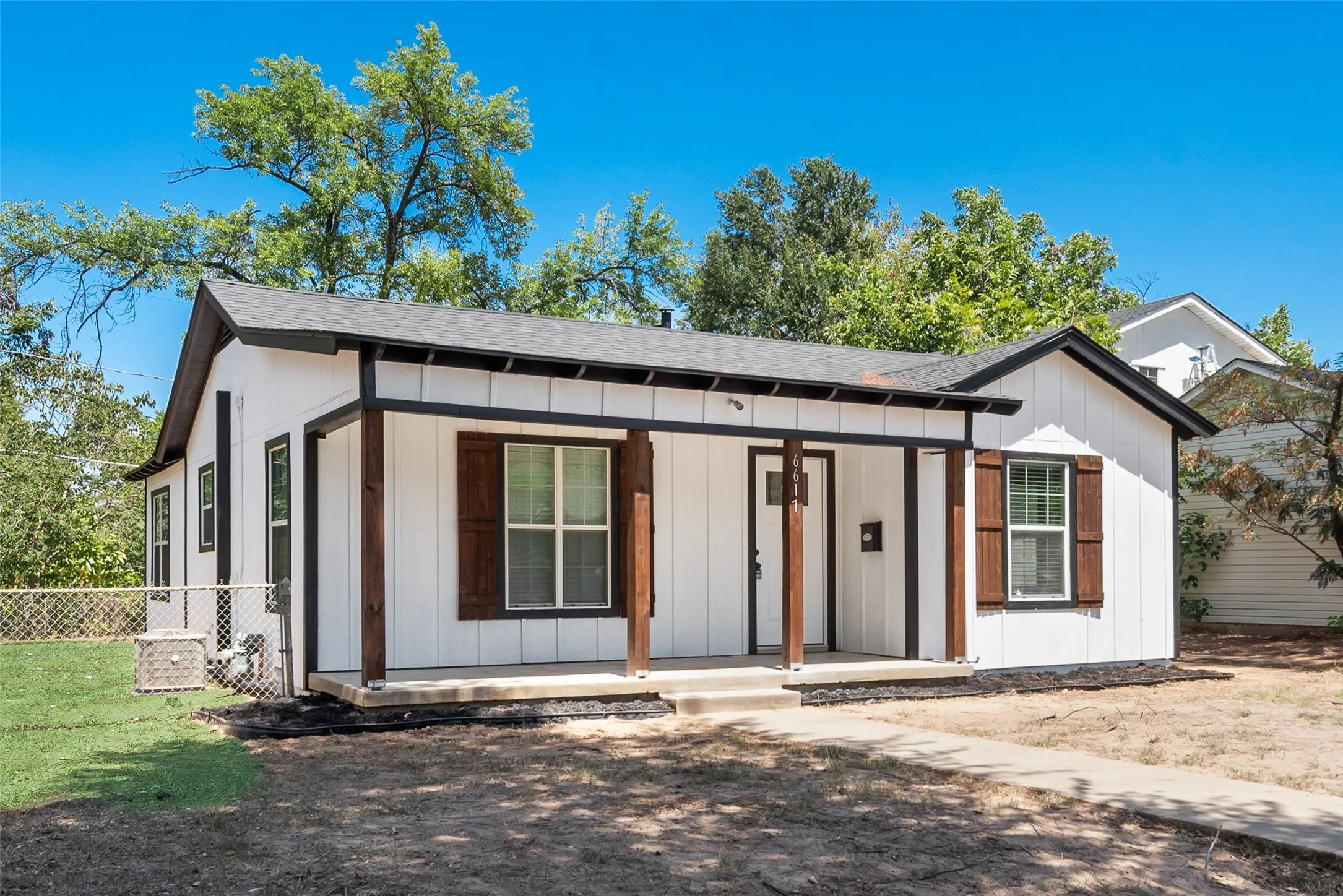 White board and batten siding, dark trim accents, covered front porch with wood columns, dark wood shutters, and a concrete walkway