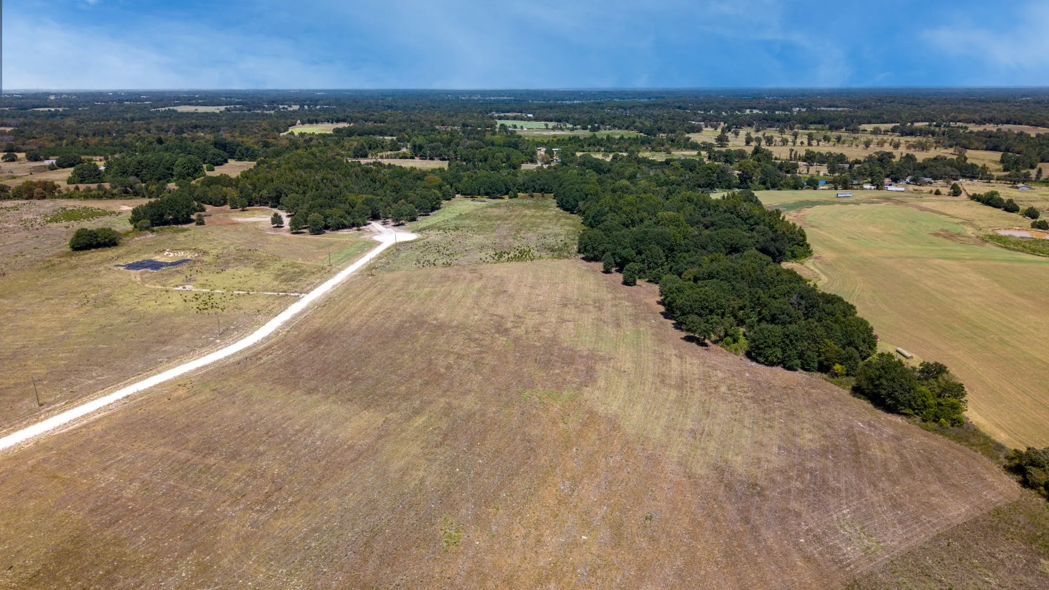 Expansive acreage featuring a winding gravel road, mature tree lines, and a visible pond