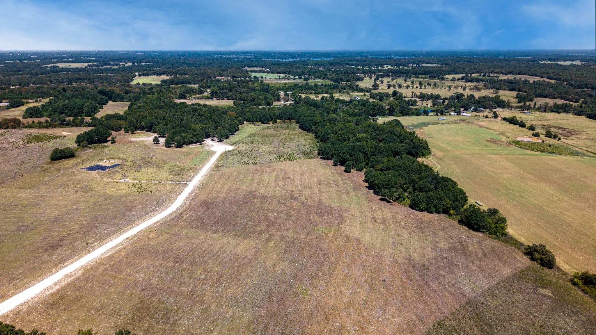 Expansive acreage featuring a private gravel driveway, wooded sections, open fields, and a small pond