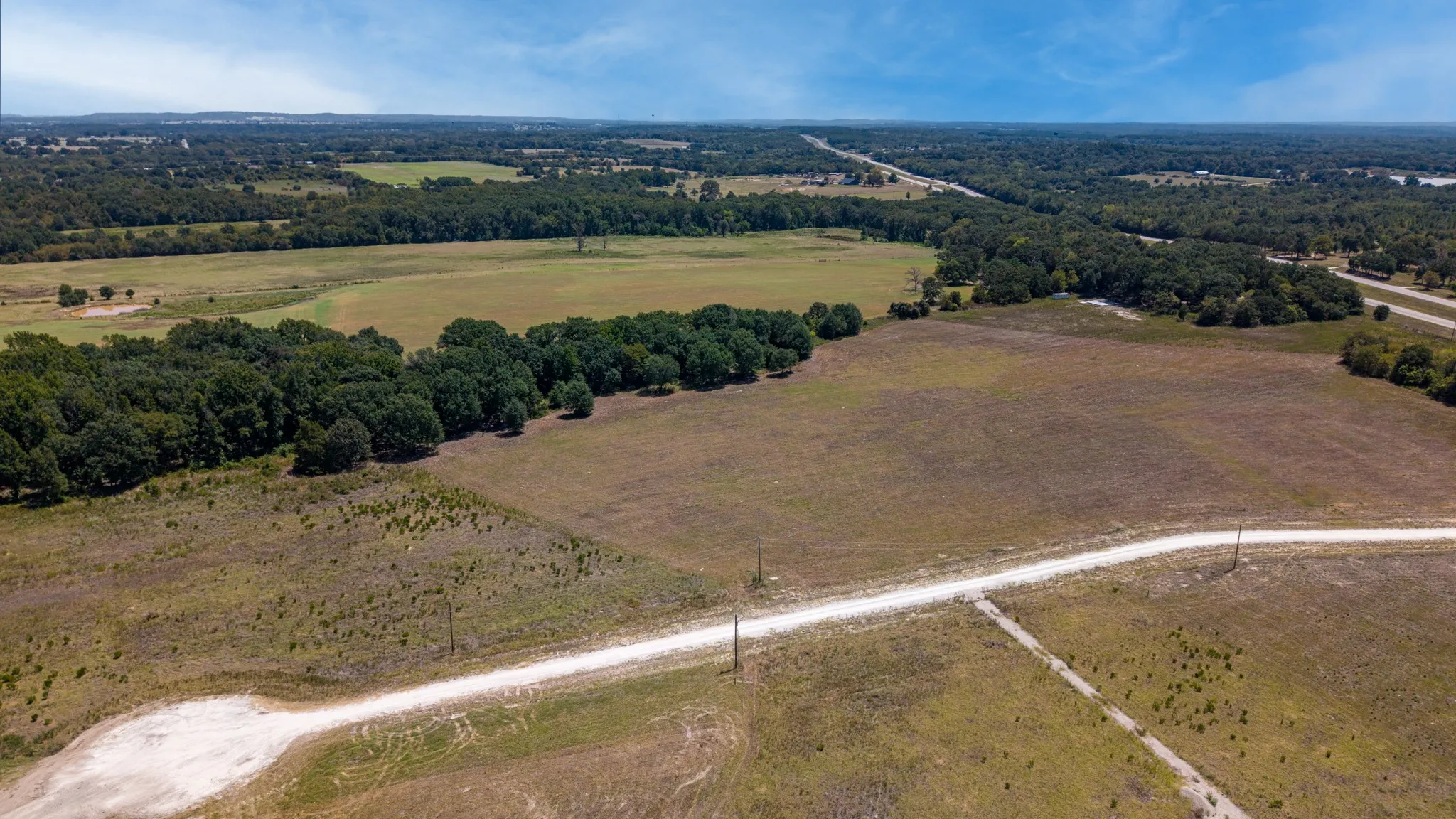 Expansive open acreage with a dirt road, surrounded by mature trees and additional clear land parcels