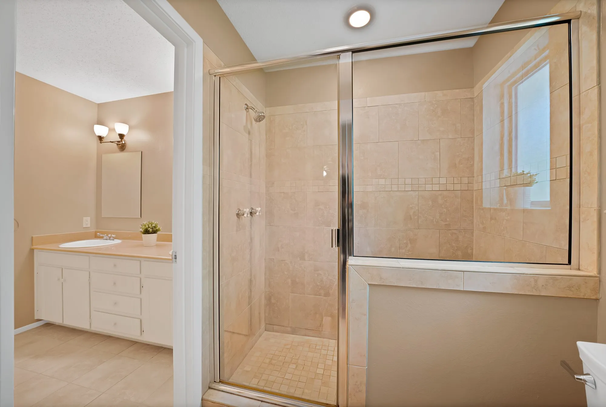 Tile-surround shower with glass enclosure, integrated window, and a separate vanity area featuring a single sink and wall-mounted lighting