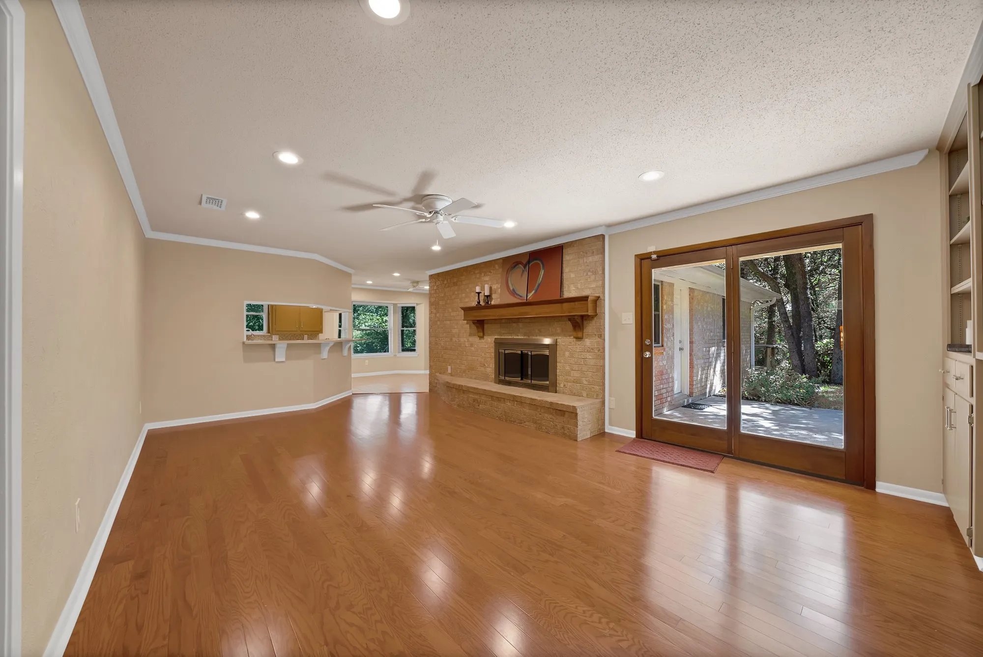 Hardwood-finish flooring, brick fireplace with mantel, built-in shelving, recessed lighting, and patio access through glass doors