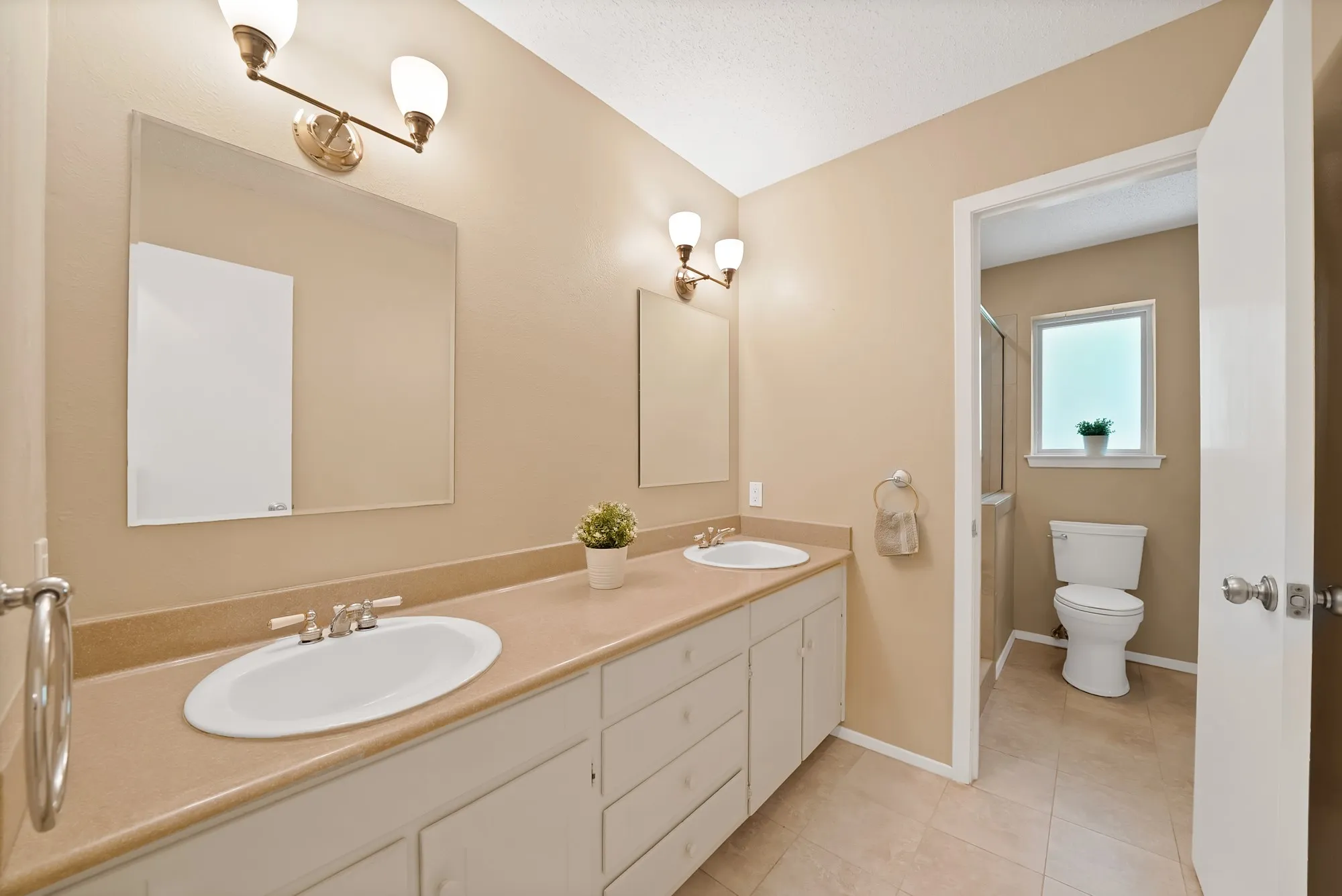 Dual vanity with integrated sinks, ample countertop space, wall-mounted light fixtures, and neutral wall tones