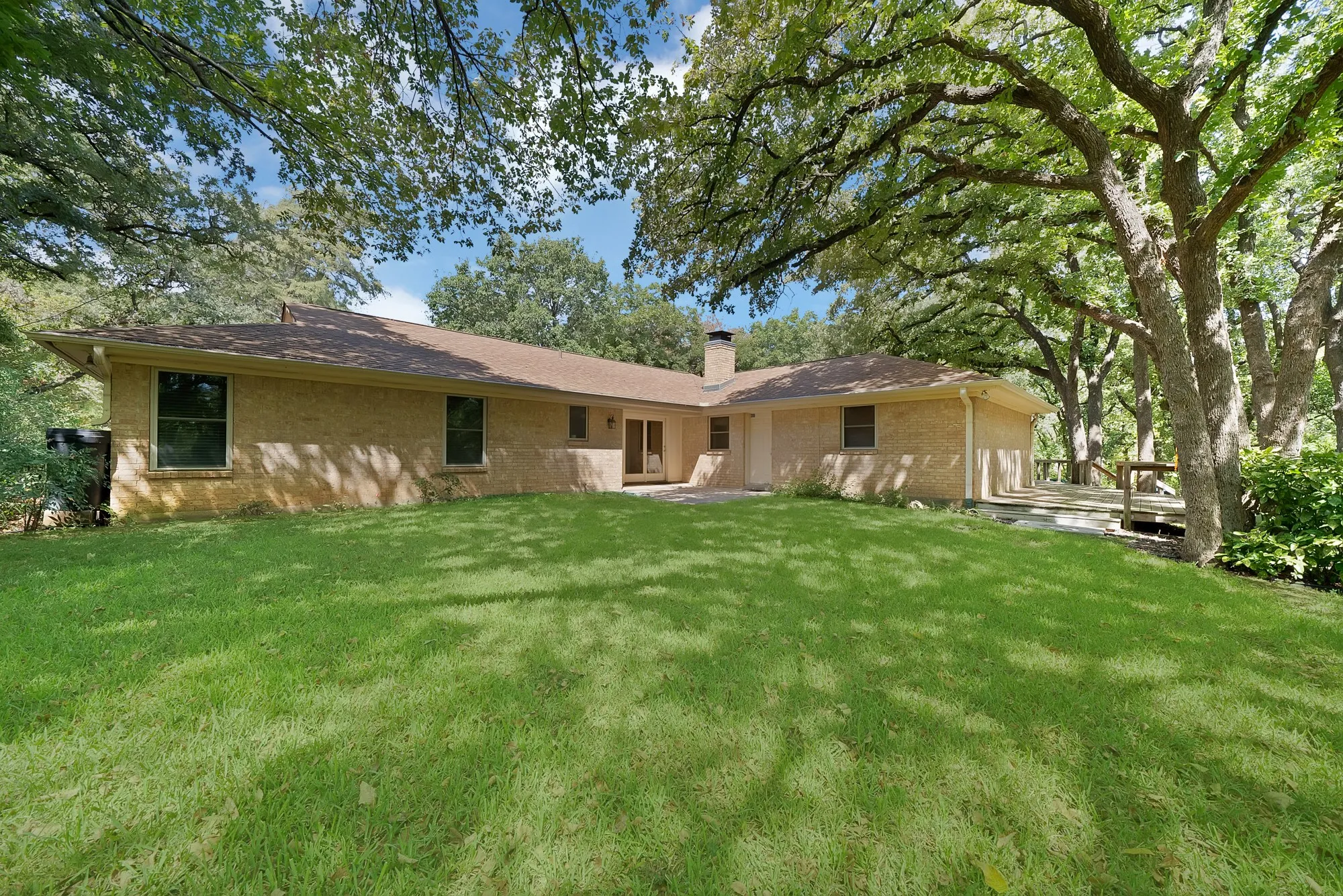 Expansive lawn with mature trees, a light brick exterior, dark-framed windows, and an outdoor patio