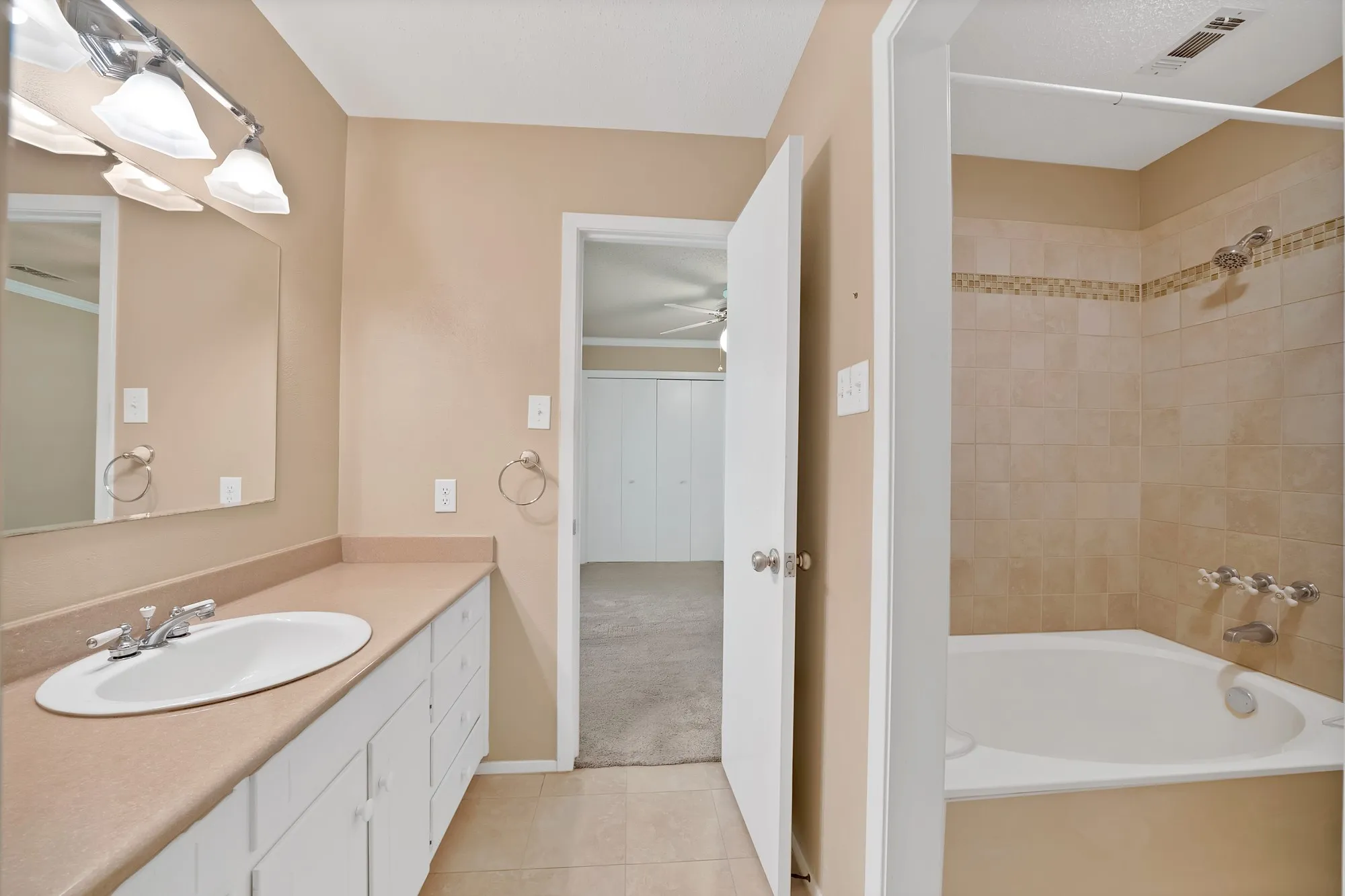 Bathroom featuring a vanity with an integrated sink, a large wall-mounted mirror, and a tiled bathtub/shower combination