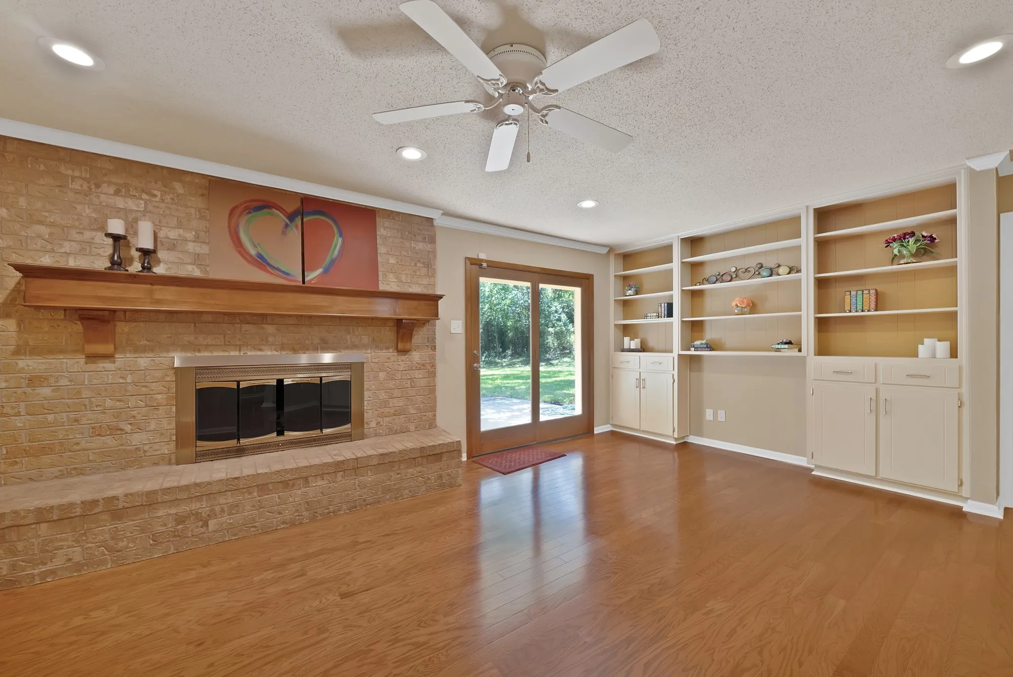 Brick fireplace with a wood-finish mantel, built-in shelving, wood-finish flooring, and sliding glass doors