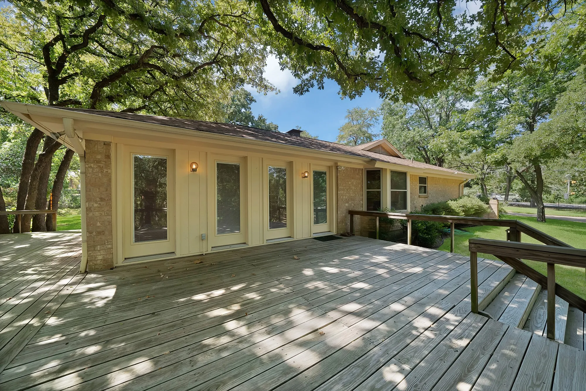 Expansive rear deck with wooden railings and steps, featuring multiple French patio doors and a stone facade