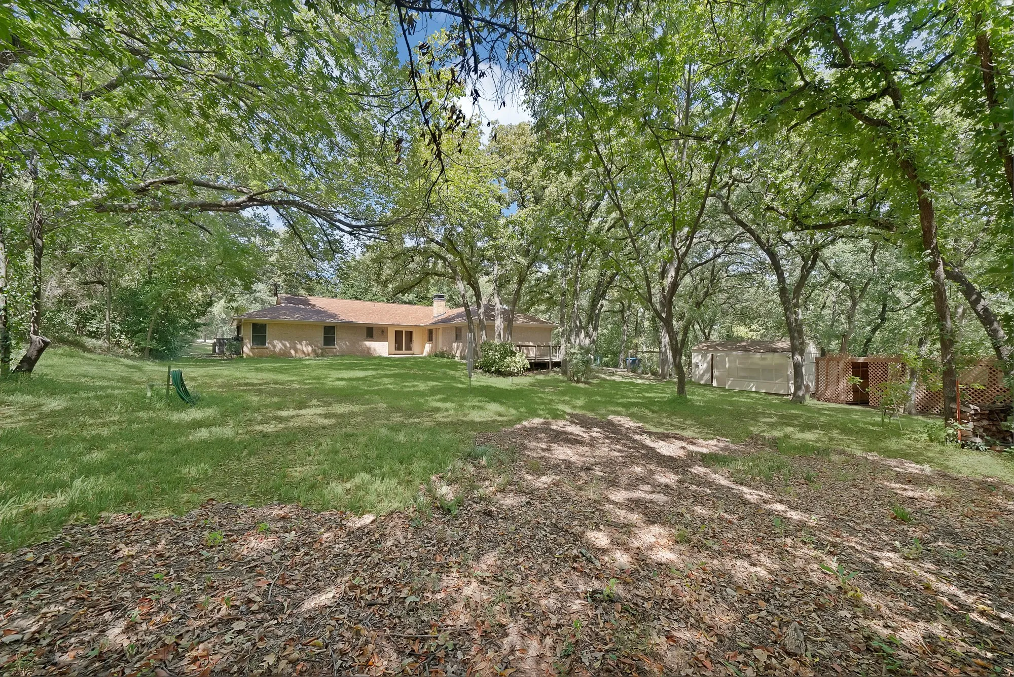 Expansive backyard with a manicured lawn, mature trees, and a brick exterior dwelling