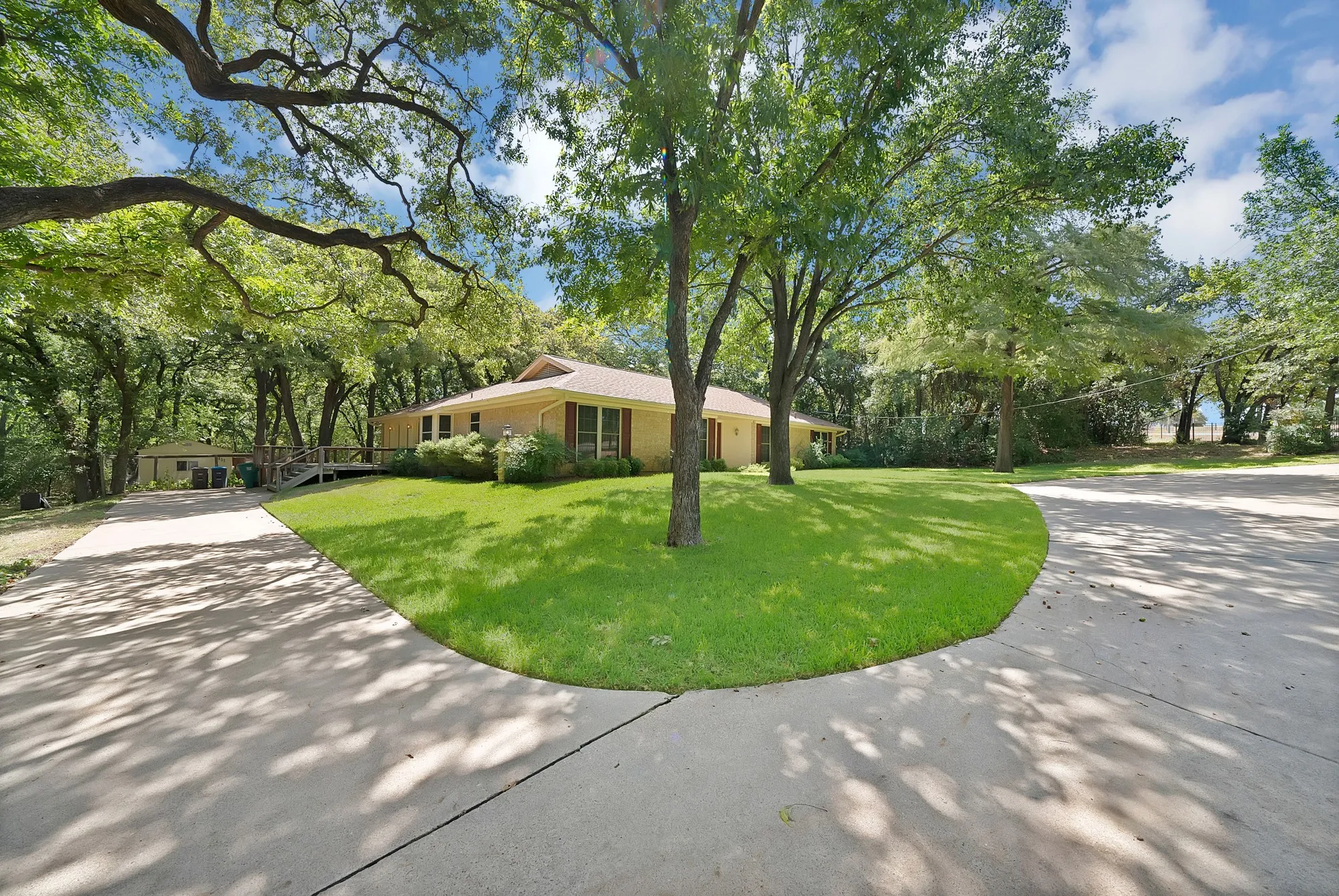 Expansive front yard with mature trees, a manicured lawn, and a wide concrete driveway