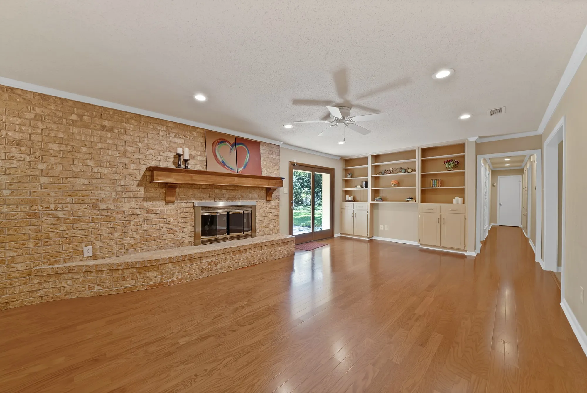 Wood-finish flooring, brick-clad fireplace with wood mantel, built-in shelving, recessed lighting, and a ceiling fan