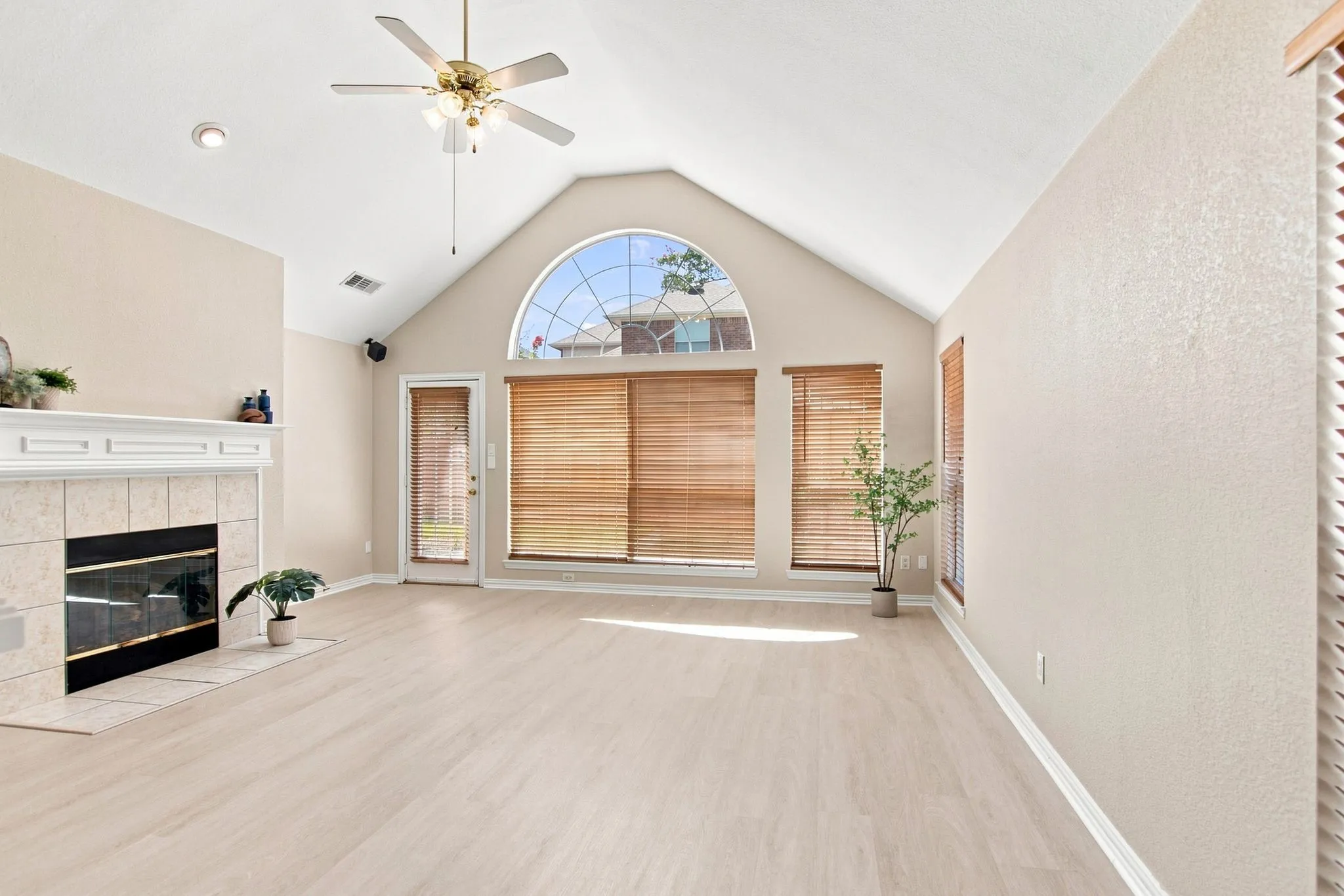 Vaulted ceilings, a tiled fireplace with a mantel, a ceiling fan with integrated lighting, wood-finish flooring, and arched window