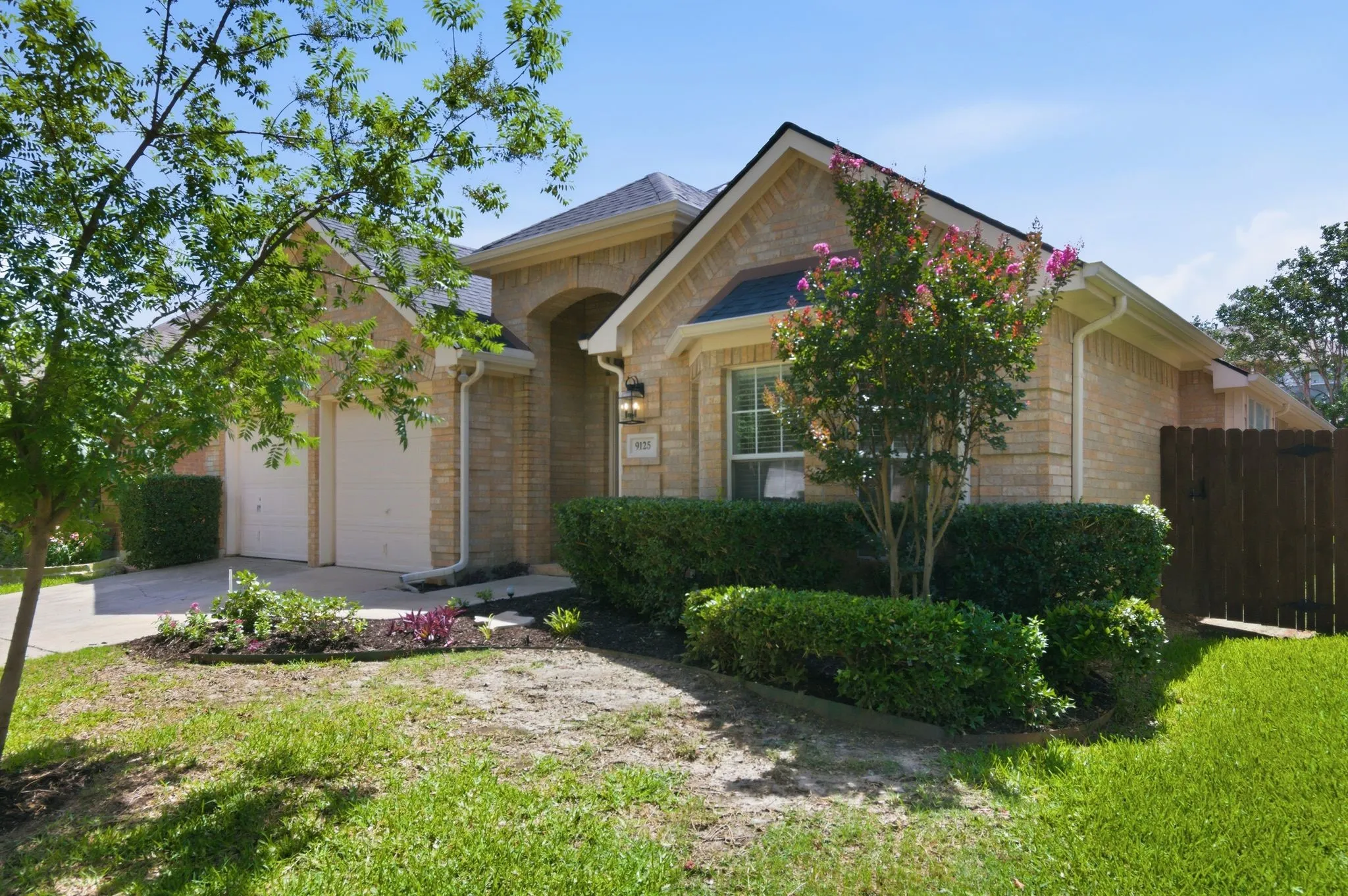 Brick facade with an arched entry, two-car garage, and mature landscaping