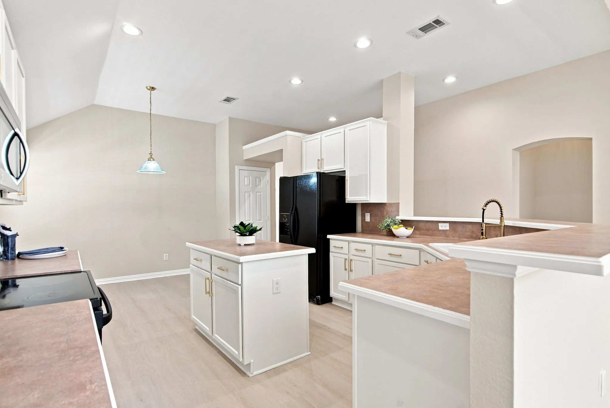 Recessed lighting, wood-finish flooring, white cabinetry, integrated kitchen island, and a gold-finish faucet