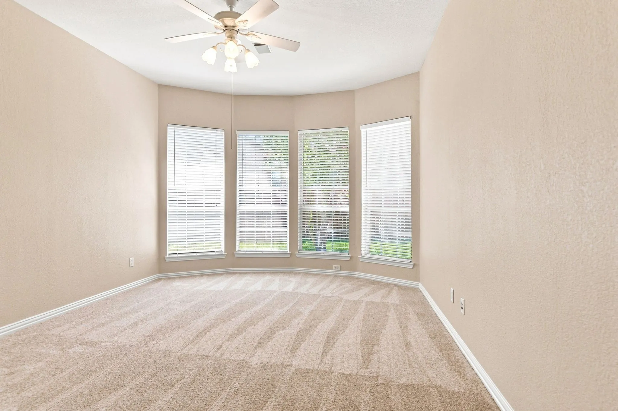 Bay window with multiple vertical blinds, neutral tone walls, recessed ceiling with a ceiling fan, and light-colored carpeting
