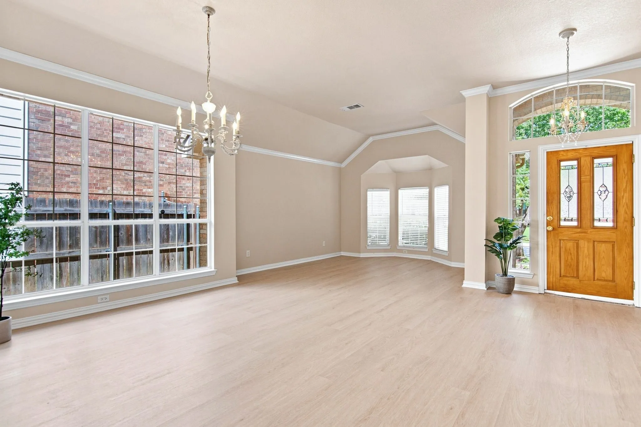 Sophisticated foyer and great room showcasing soaring ceilings with crown molding, elegant chandelier, and light wood-finish flooring throughout