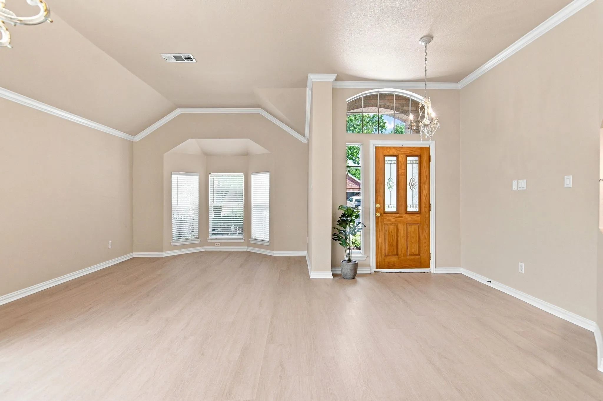 Wood-finish flooring, bay window, vaulted ceiling, crown molding, and a decorative front door with transom window
