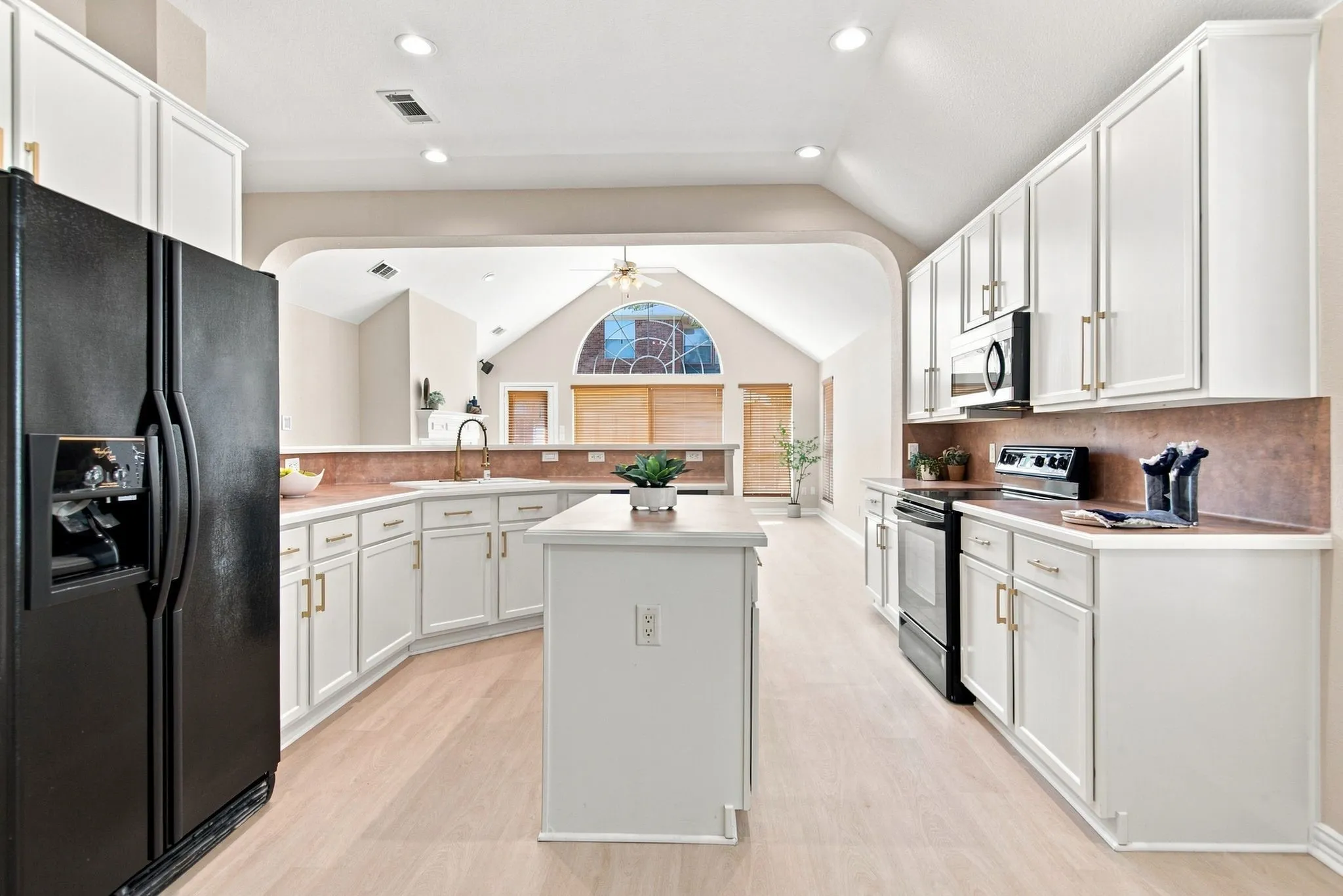 Spacious kitchen featuring white cabinetry, a central island, black appliances, and light wood-finish flooring