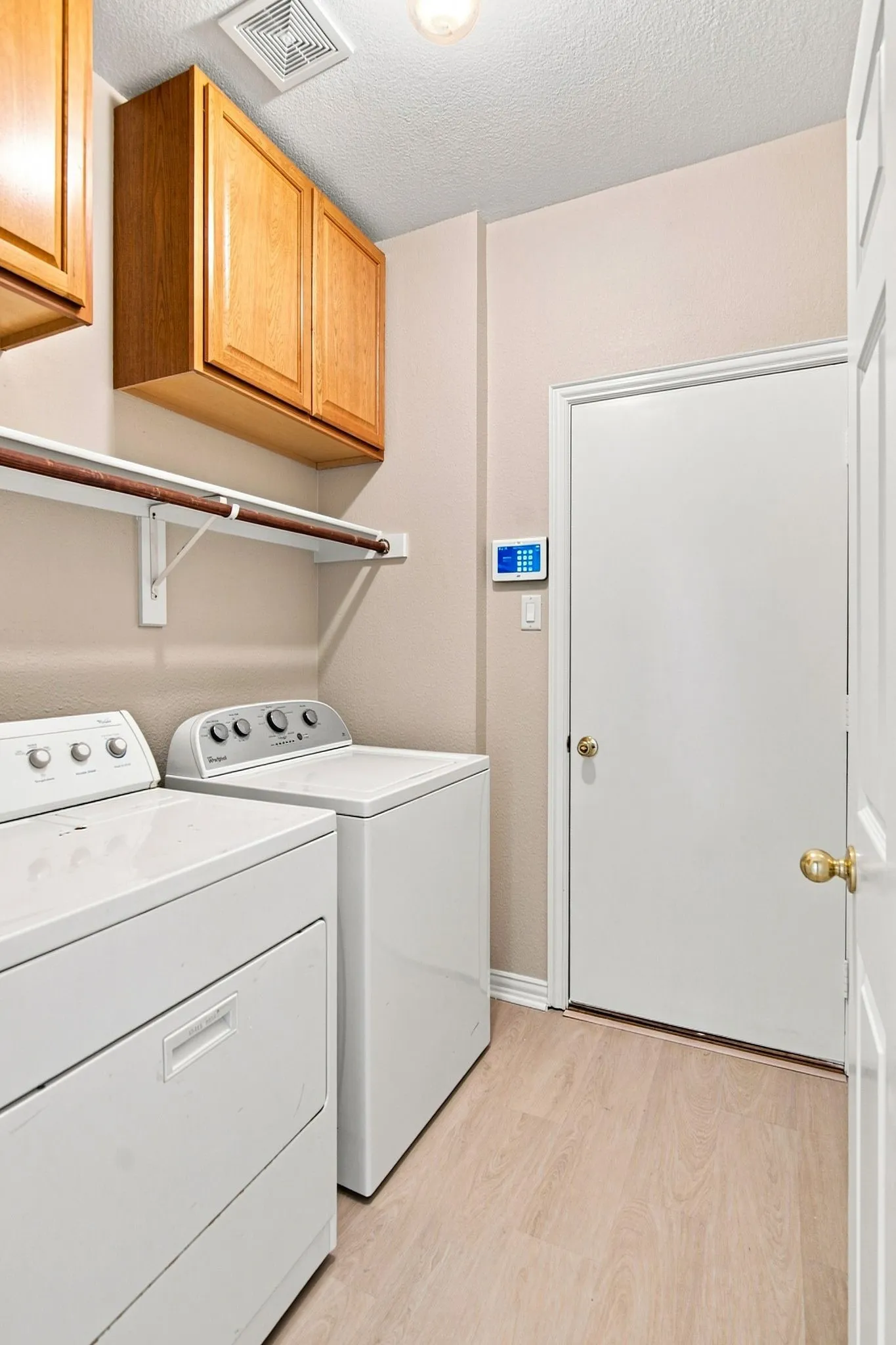 Laundry area featuring wood-finish flooring, overhead cabinetry, and a hanging rod