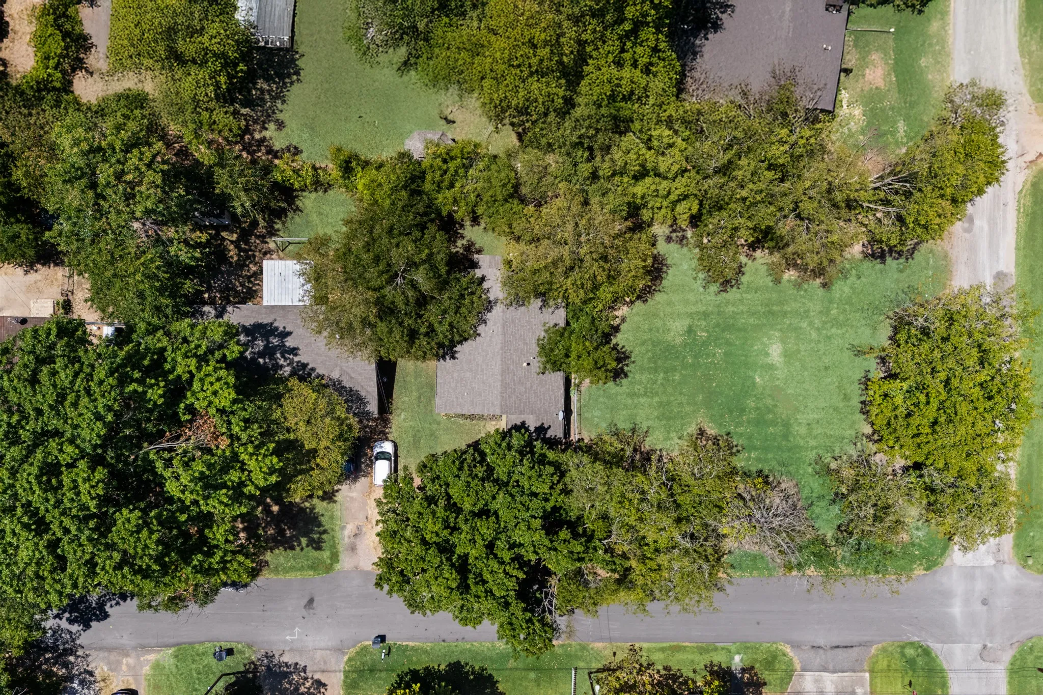 Residential property with mature trees, green lawns, and paved roads