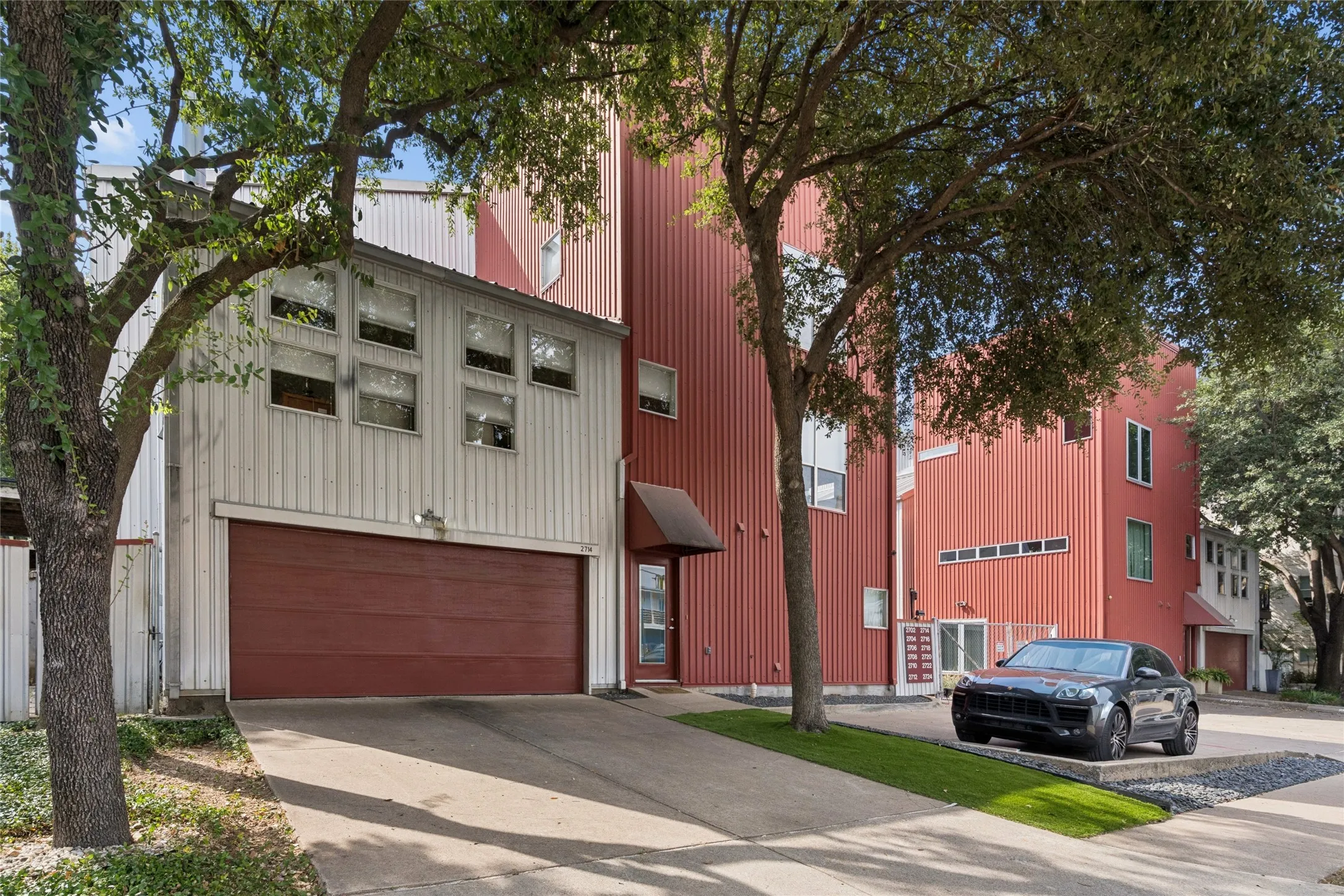 Corrugated metal siding, attached garage, multiple windows, concrete driveway, and established trees