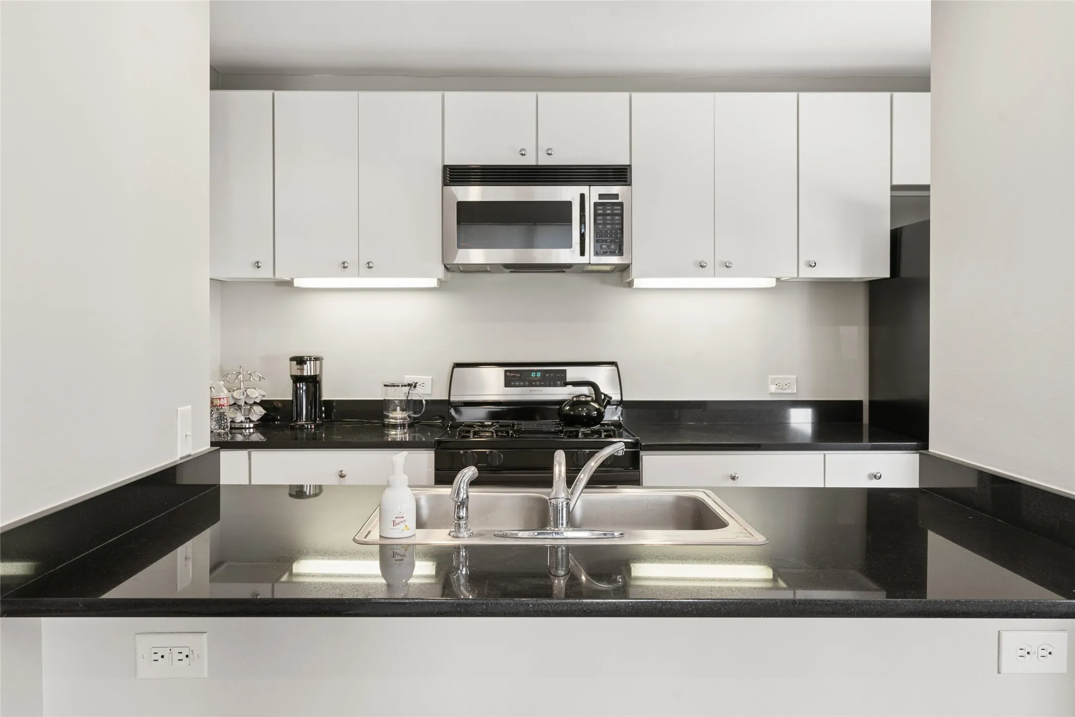 Kitchen featuring black countertops, stainless steel sink, gas range, microwave, and white cabinetry