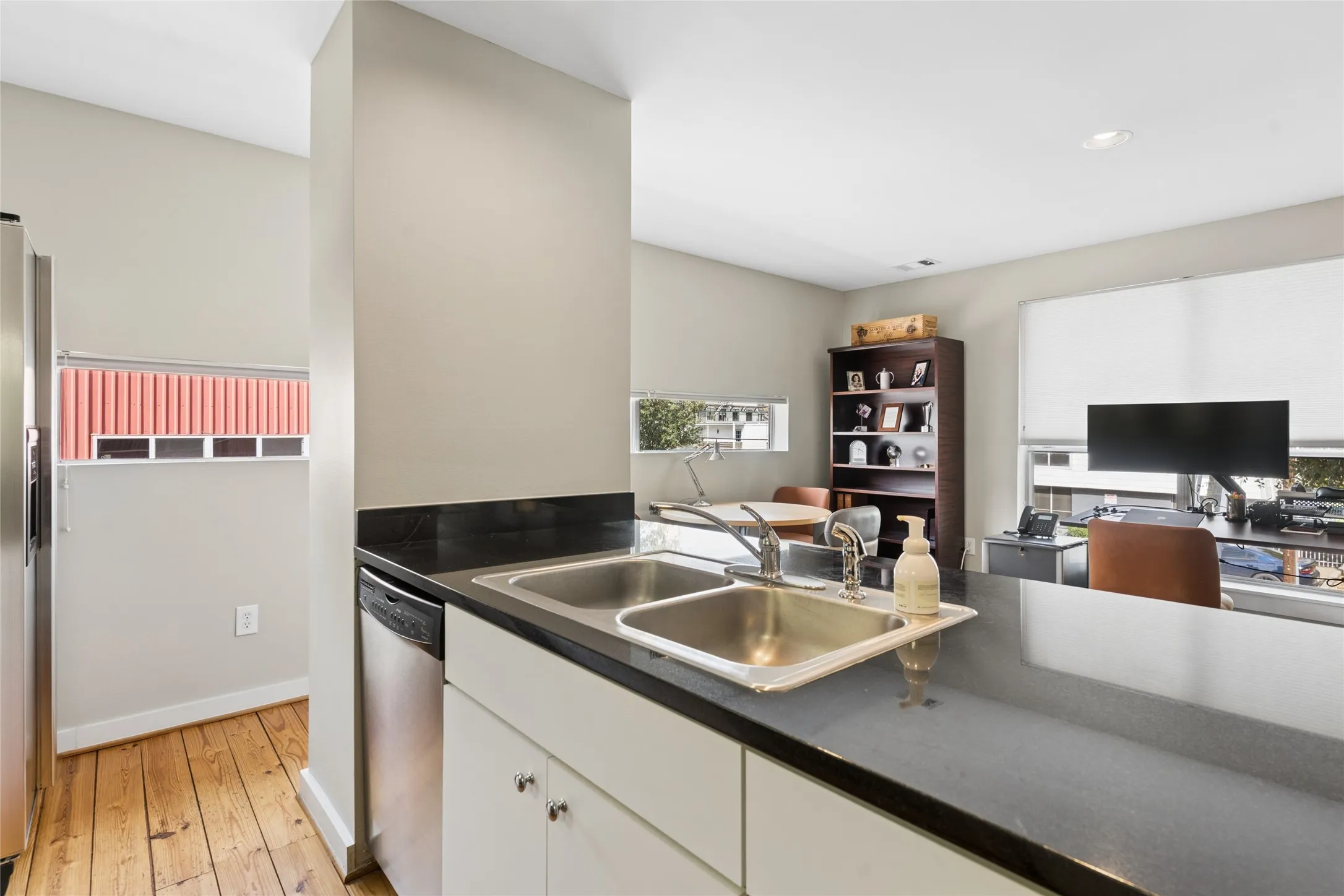 Kitchen featuring a double basin stainless steel sink, dark countertops, white cabinetry with silver hardware, and a stainless steel dishwasher
