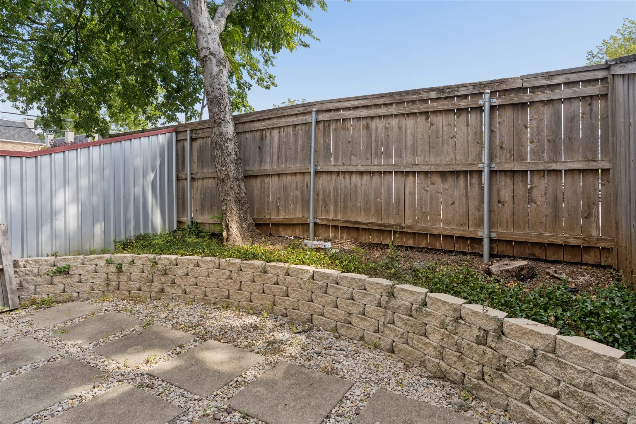 Paved patio area featuring large square pavers, gravel accents, and a stone retaining wall