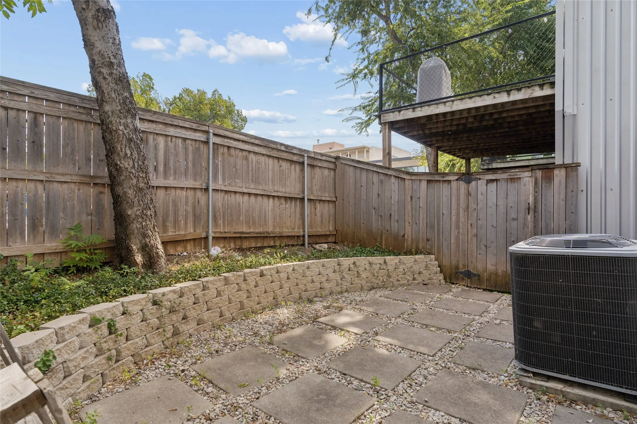 Private outdoor space featuring stone paver patio and retaining wall, wood fencing, and a permanent elevated deck structure