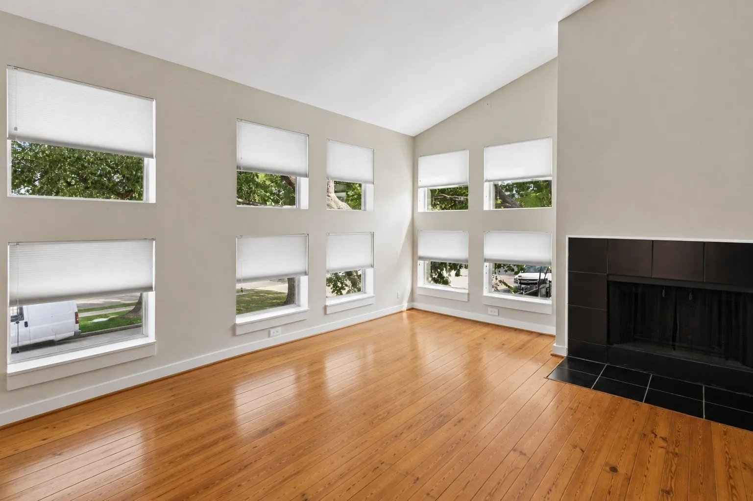 Vaulted ceilings, wood-finish flooring, multiple windows, and a black tile fireplace with a hearth