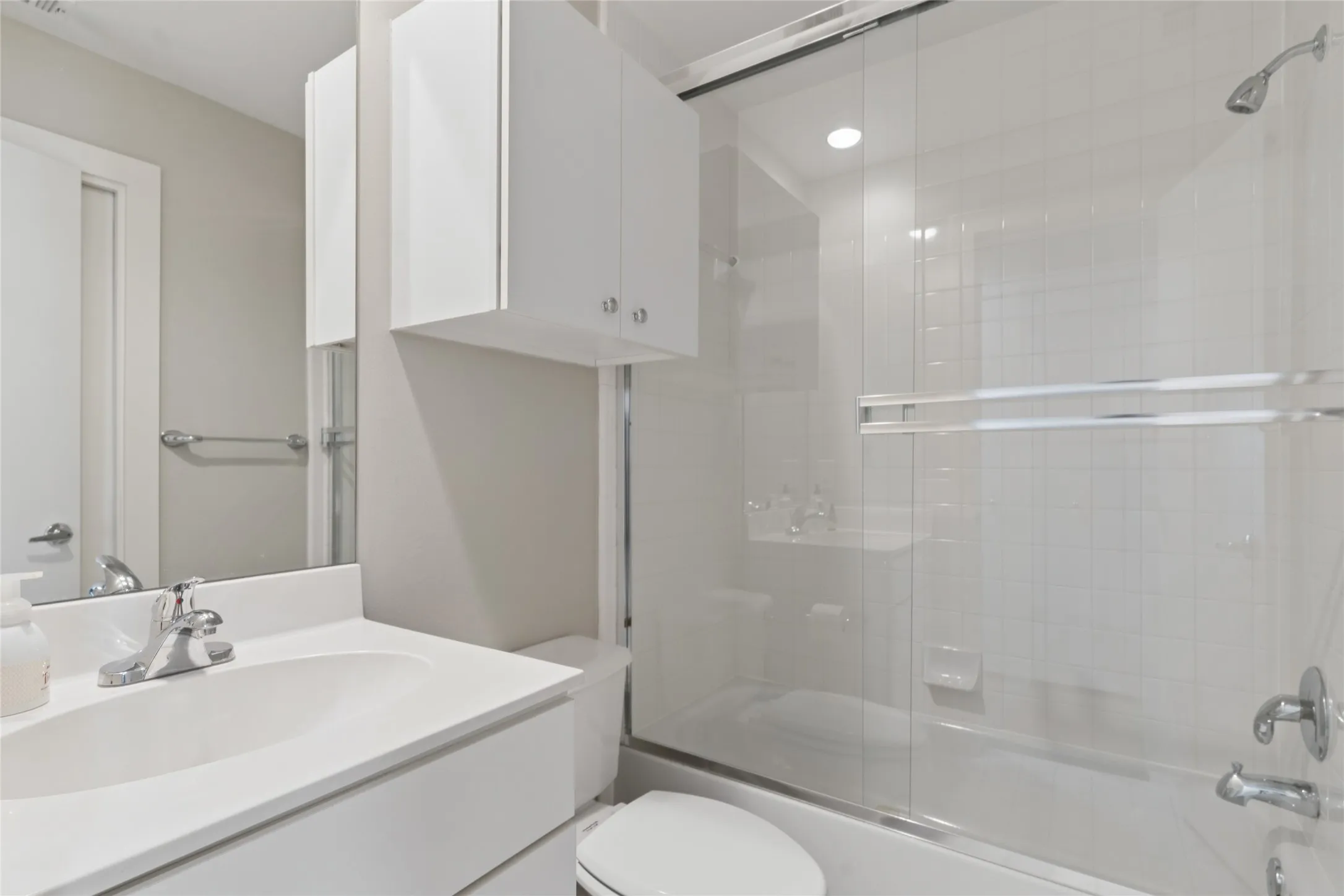 Bathroom featuring a vanity with an integrated sink, polished chrome faucet, white cabinetry, and a shower-tub combination with a sliding glass enclosure