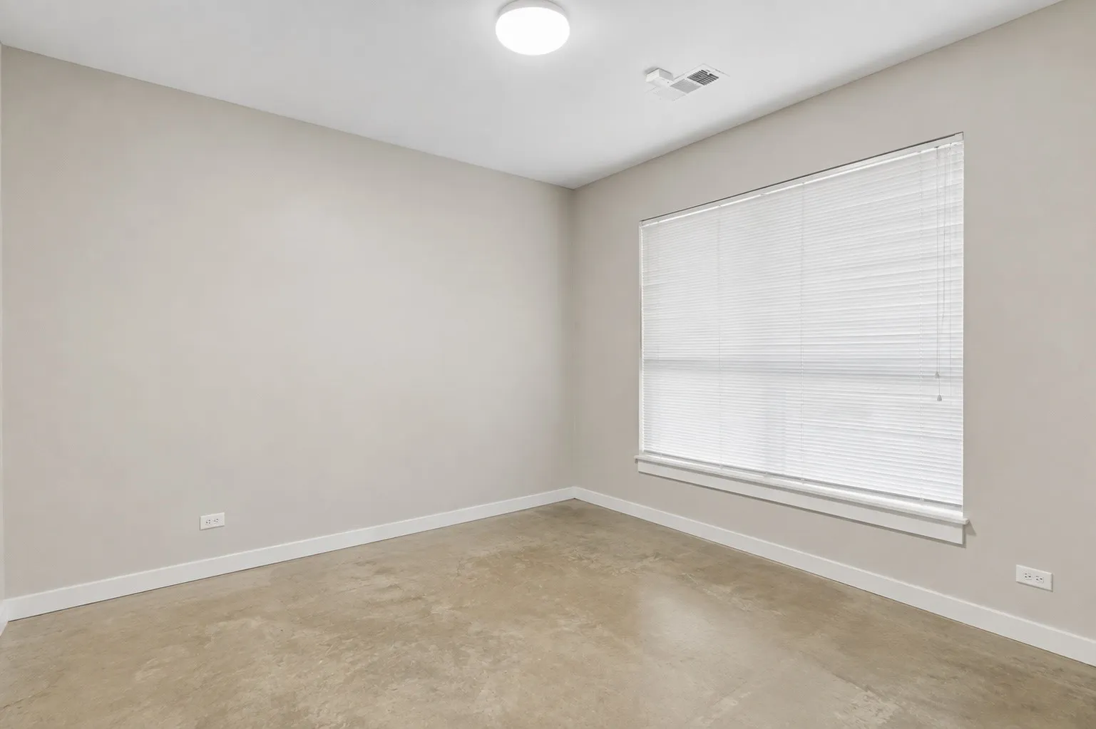 Neutral wall color, concrete-finish flooring, large window with blinds, ceiling-mounted light fixture, white trim