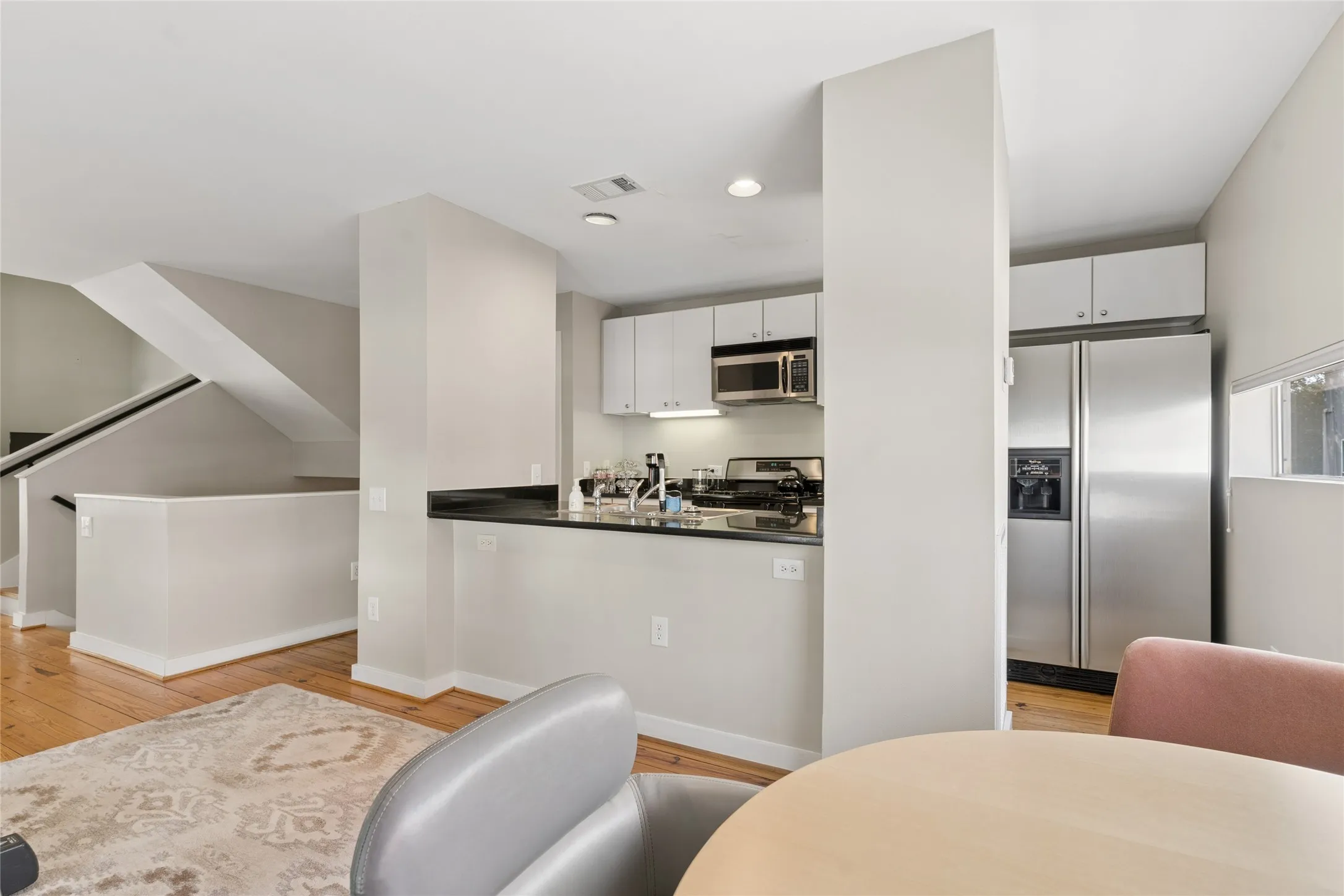 Hardwood flooring throughout, contemporary kitchen with stainless steel appliances, white cabinetry, dark countertops, and a built-in microwave