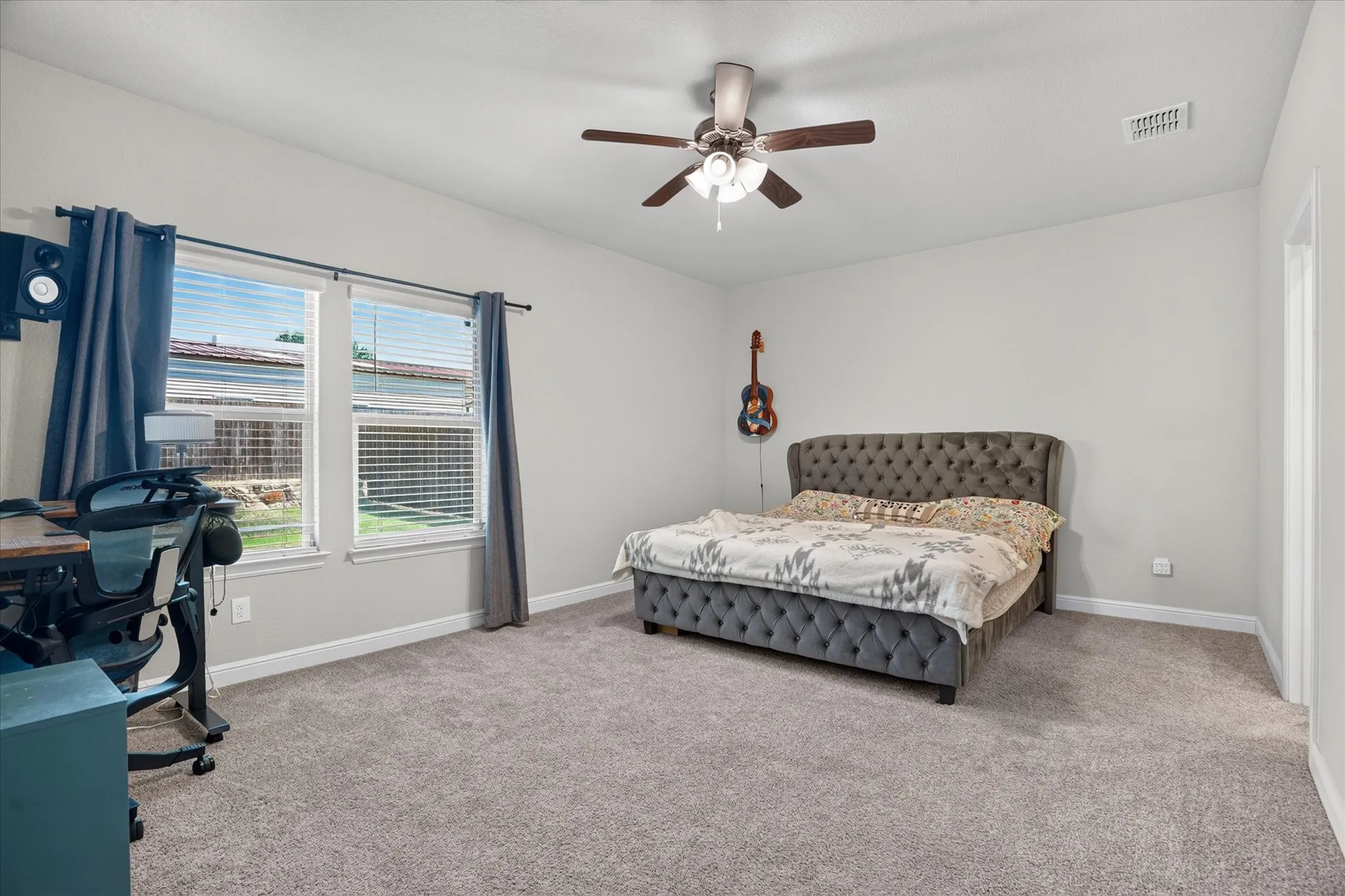 Carpeted flooring, white walls, two large windows, and a ceiling fan with integrated lighting