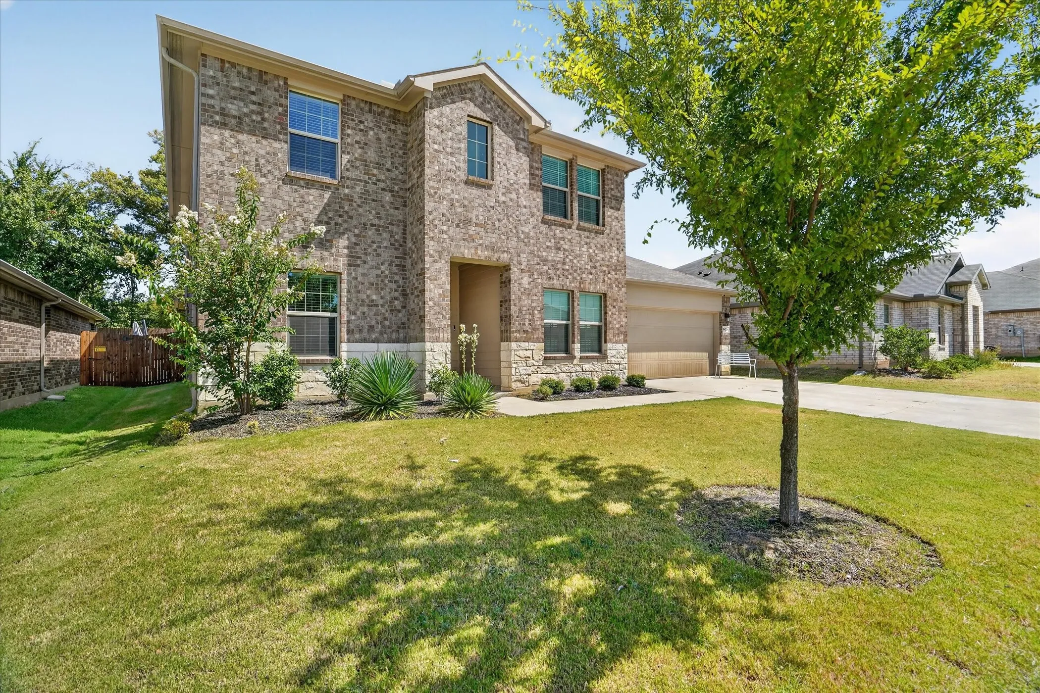 Brick and stone facade, two-story structure, attached garage, well-maintained lawn, established landscaping