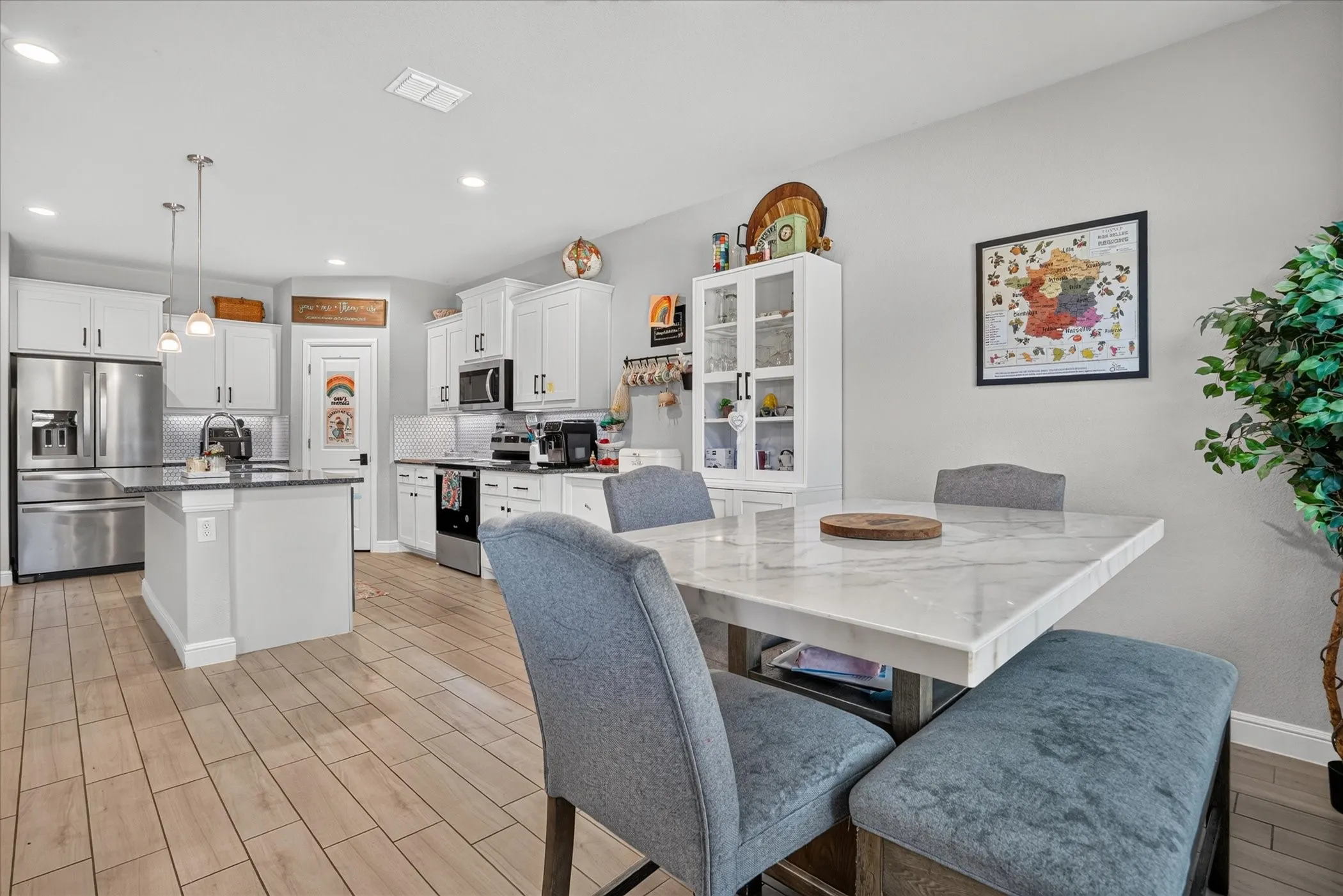 White shaker cabinetry, stainless steel appliances, wood-finish tile flooring, recessed lighting, and a kitchen island with pendant lighting