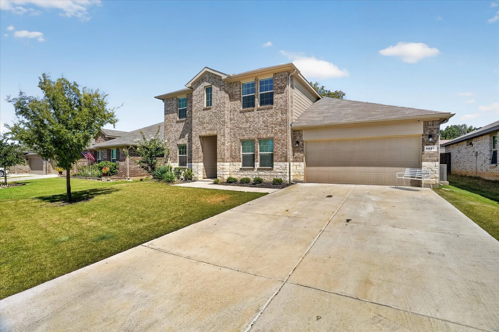 Brick and stone facade, multi-story structure, attached two-car garage, concrete driveway, and front lawn