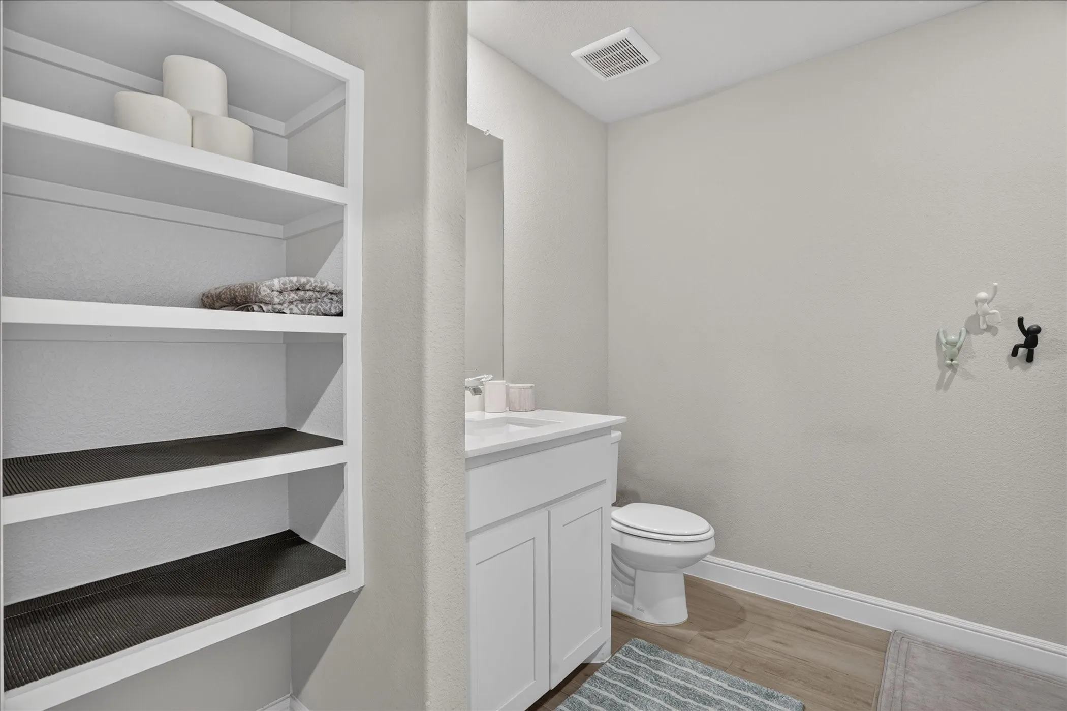 Built-in shelving, wood-finish flooring, white vanity with integrated sink, and a commode