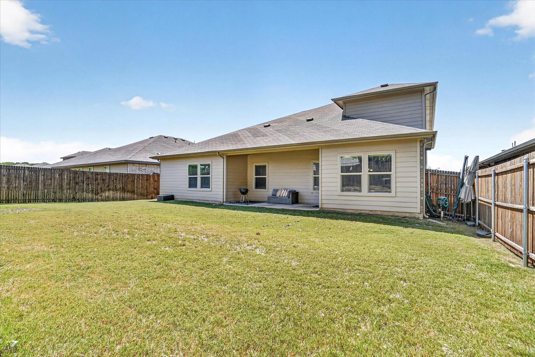 Expansive backyard featuring a covered patio, tan siding, and a privacy fence