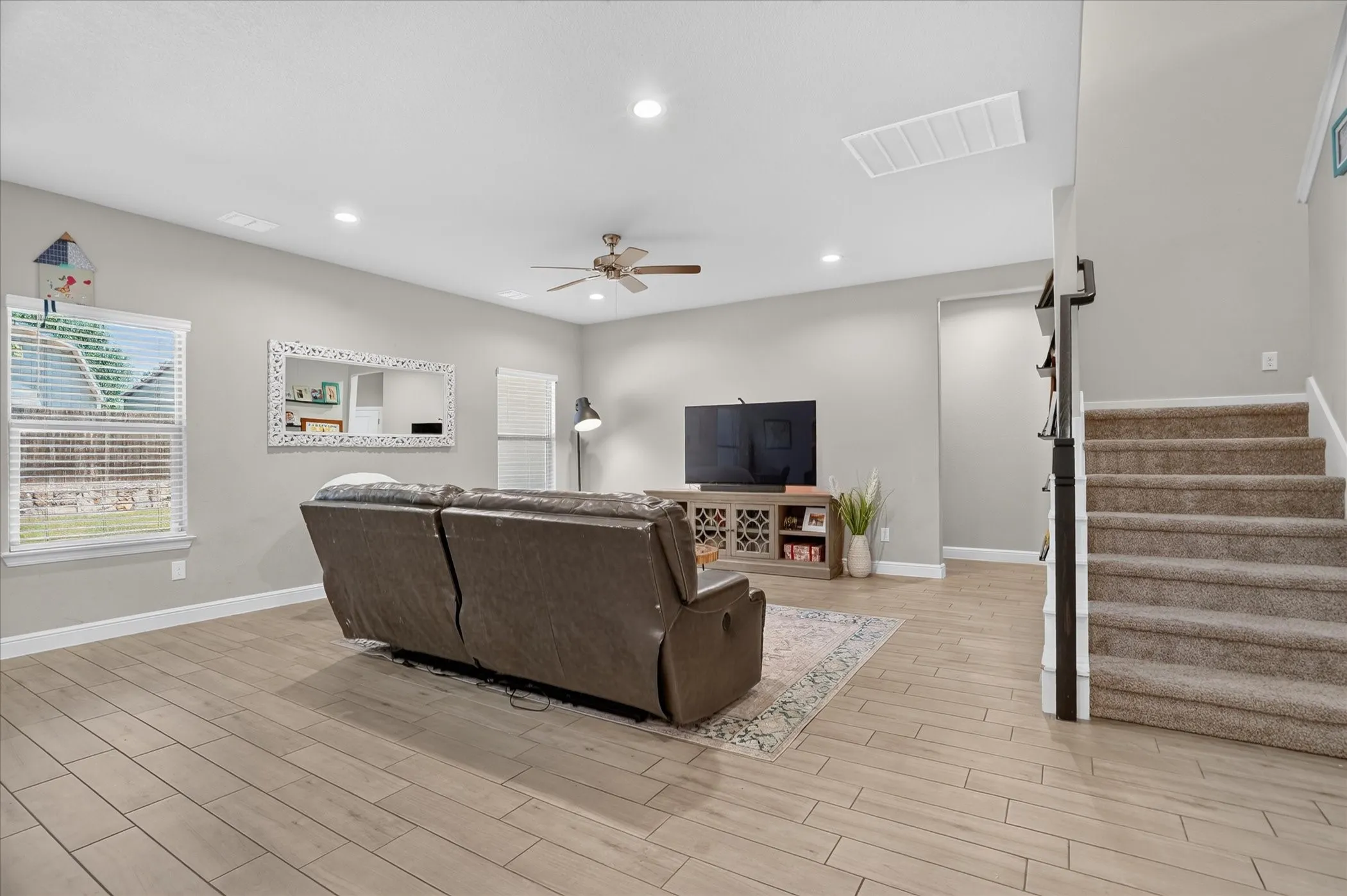 Spacious living area featuring wood-finish flooring, recessed lighting, ceiling fan, and carpeted stairs