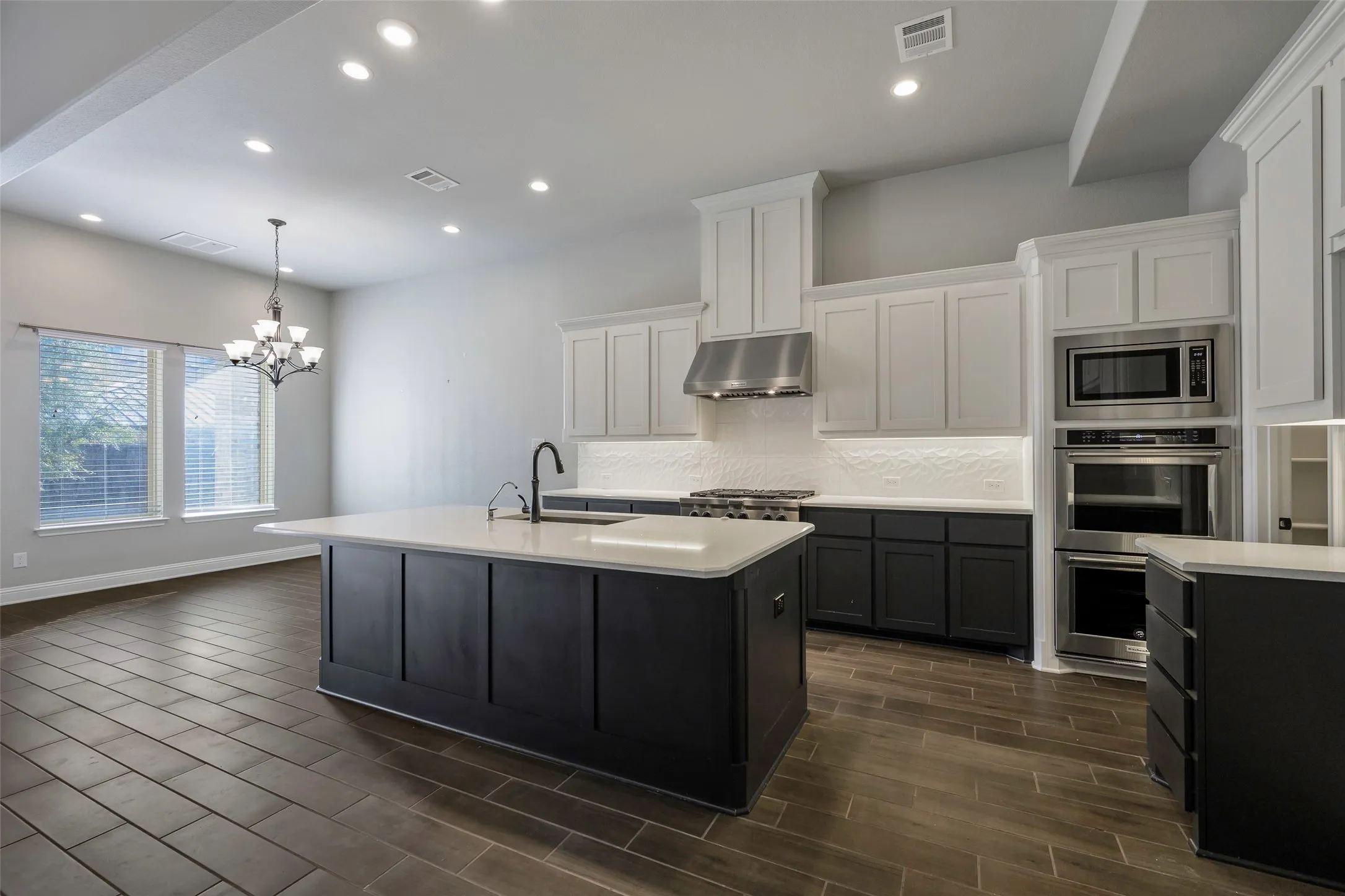 Open-concept kitchen with a central island, recessed lighting, stainless steel appliances, white subway tile backsplash, and wood-finish flooring