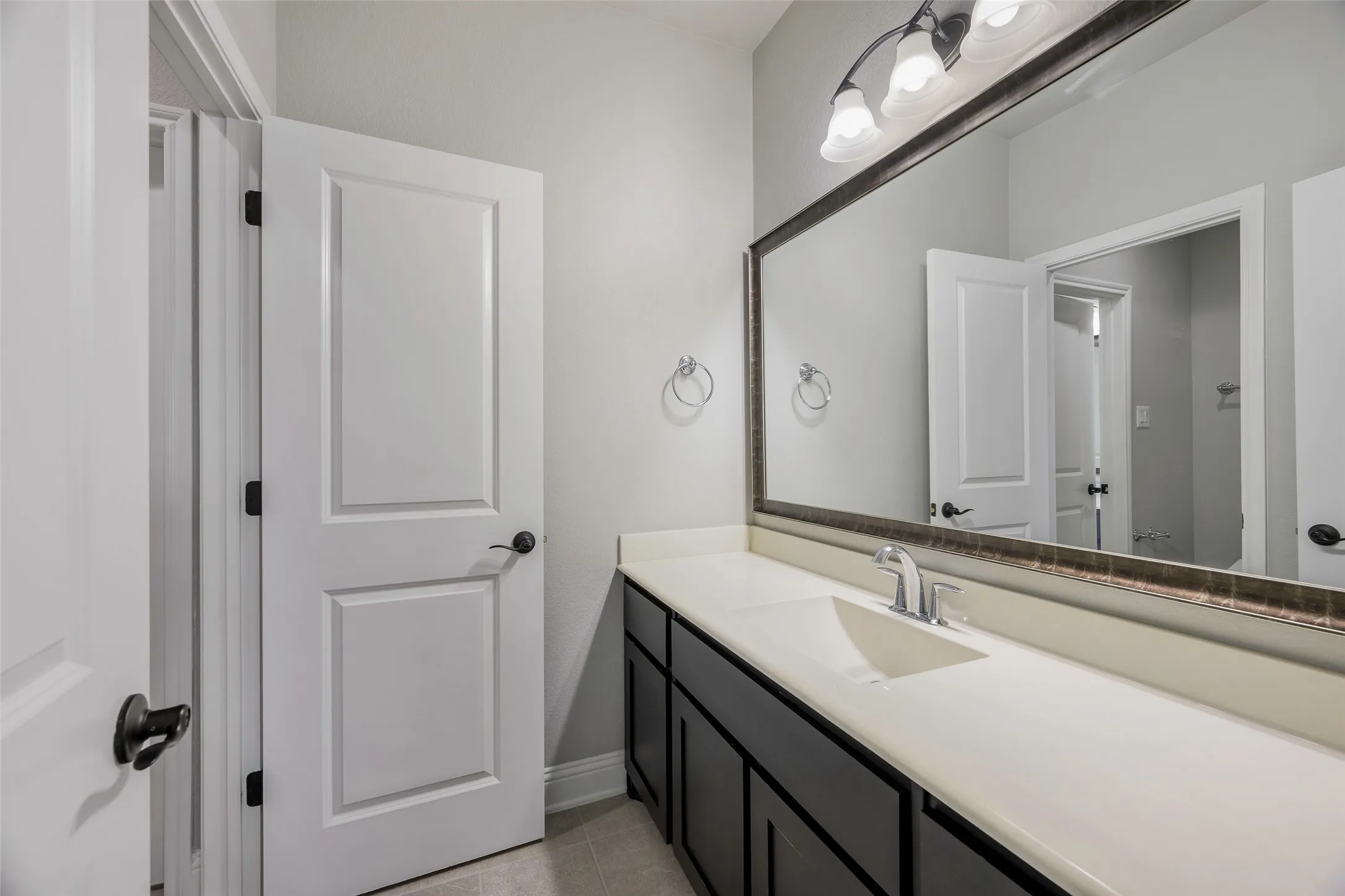 Extended vanity with an integrated sink, polished chrome faucet, dark cabinetry, and a large framed mirror