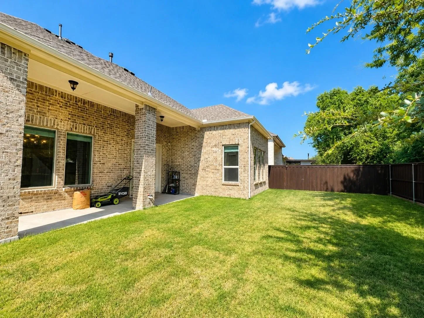 Expansive lawn area, brick exterior, covered patio, multiple windows, and a wood privacy fence